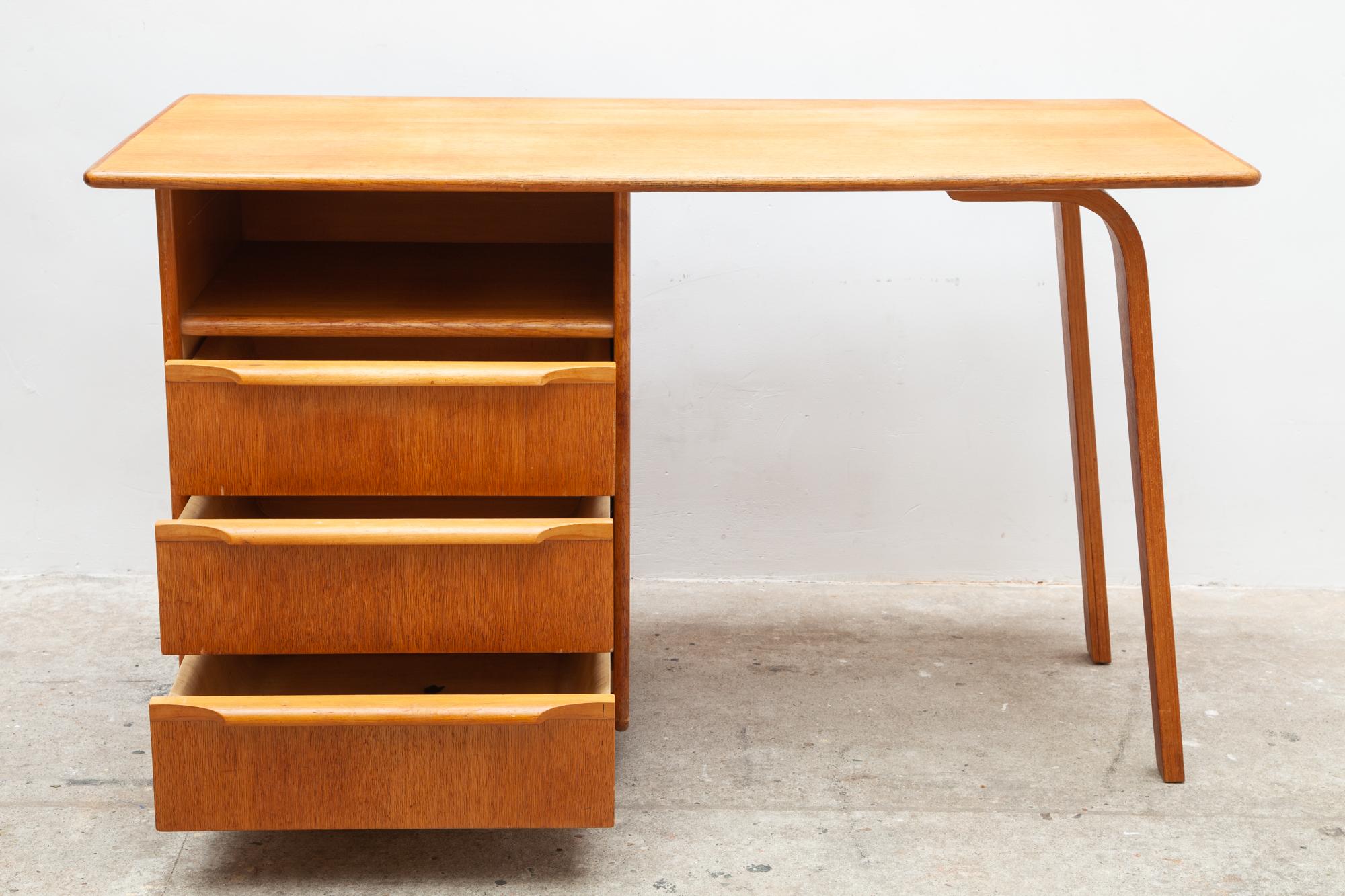 Beautiful Dutch design writing desk in oak veneer with two sculptural plywood legs and under the three chest of drawers and a shelf with the anti-dust drawers four wedge-shaped legs. The design of this vintage desk, type EE02 from the oak series is