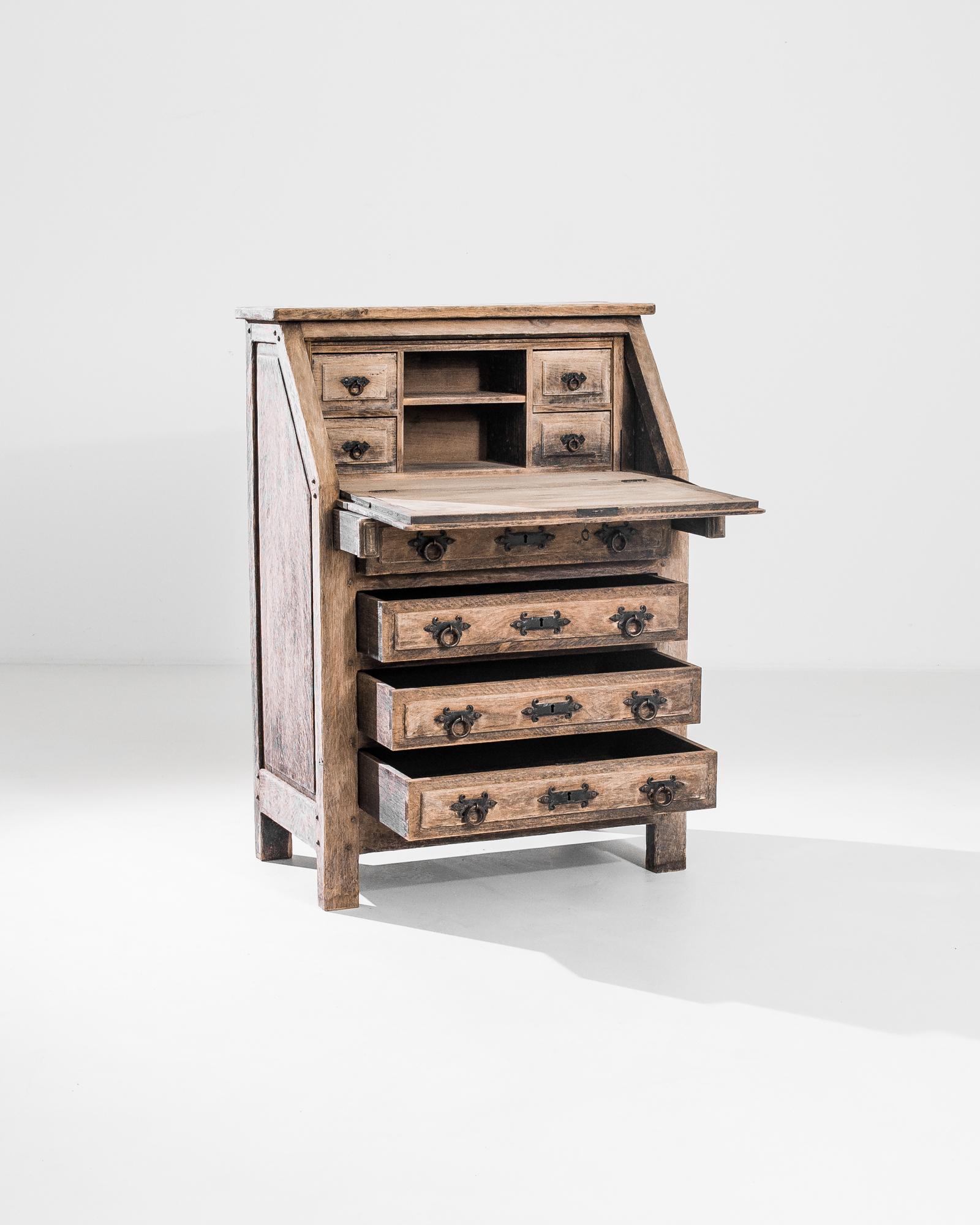 Intriguing complexity of form characterizes this desk crafted in Belgium in the 1970s. This bleached oak chest adopts an unconventional geometric shape with four drawers and a downward top door that hides six extra compartments. Original iron