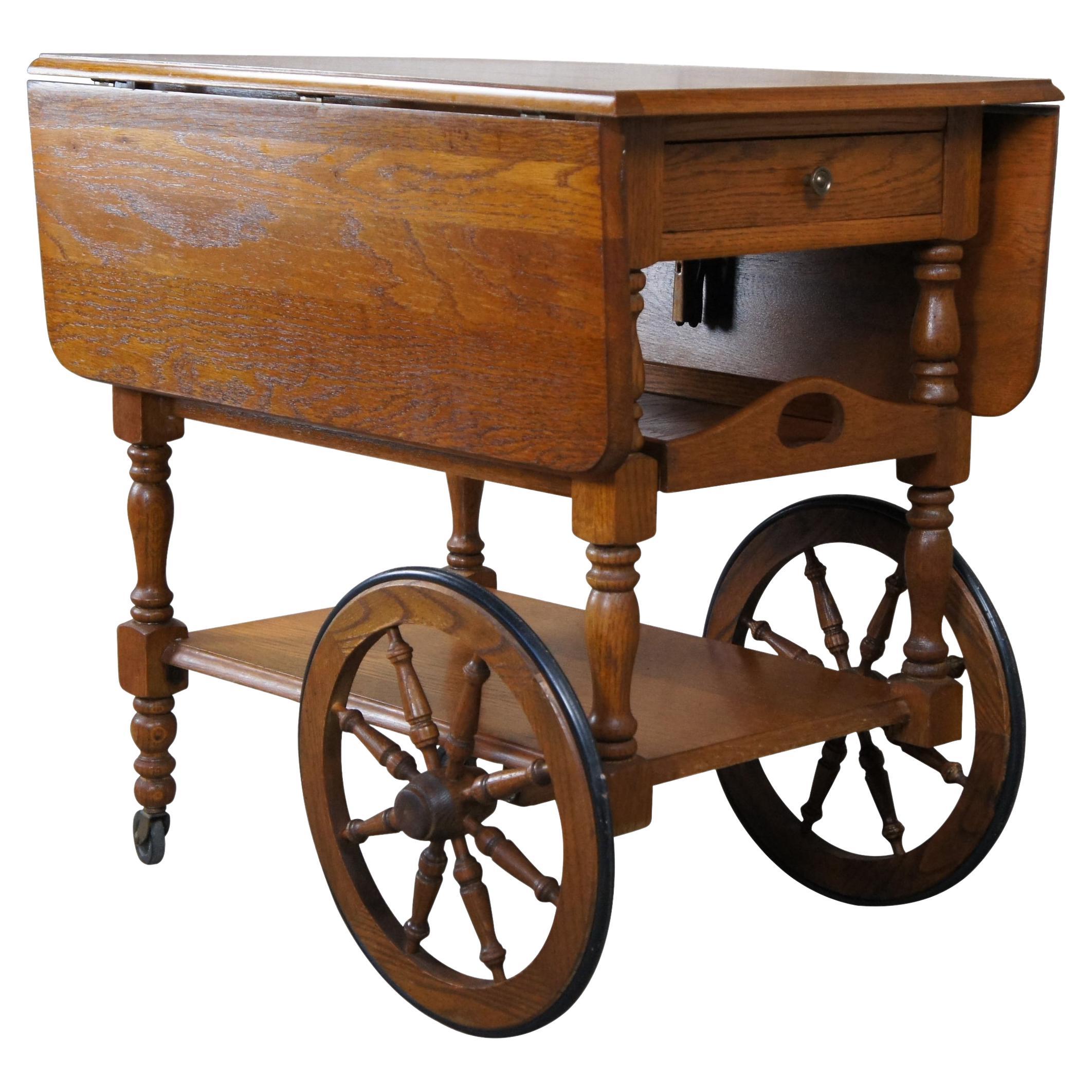 Mid 20th Century bar or tea cart. Made from oak with French Brittany styling. Includes drop leafs, dovetailed drawer and pull out drink serving tray. Features wagon wheel design and neatly concealed handle. 

Measures: 30