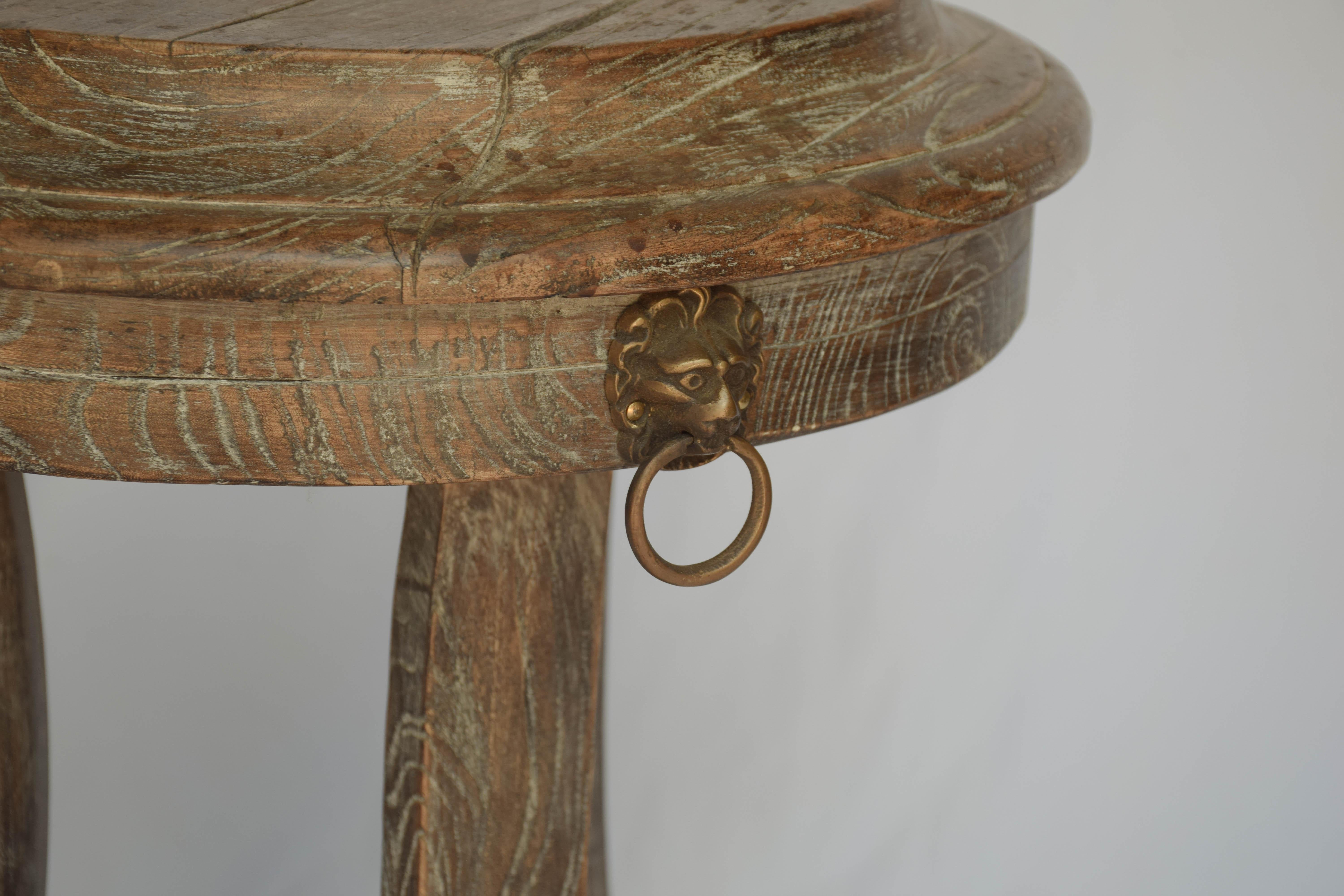 This is a vintage oak pedestal table with brass lion heads on three sides. The three legs stand on a wooden triangular shape base. The table features a washed painted patina. The size makes it perfect for a side, end or drinks table.