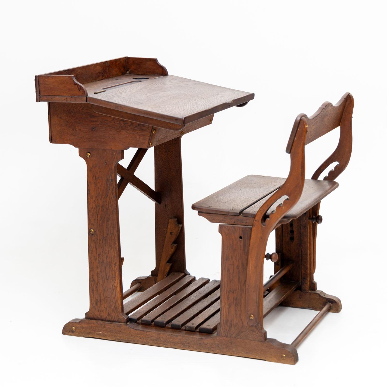 Vintage wooden school desk featuring a hinged writing surface equipped with a recessed holder for pens and inkwell. The school bench is thoughtfully designed with adjustable slats at the bottom for a comfortable footrest, and its height is also