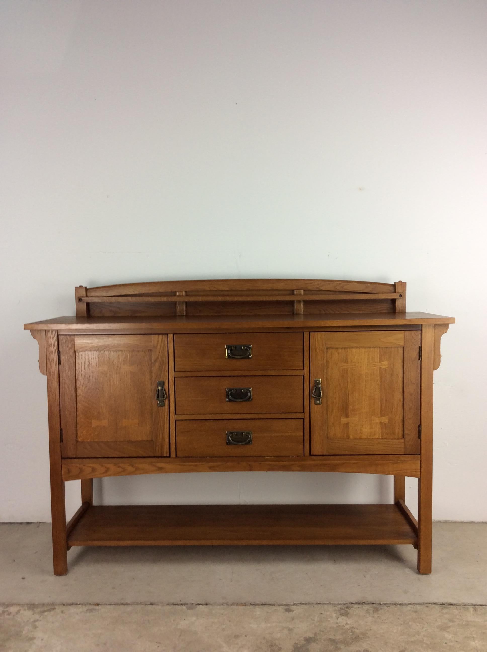This vintage sideboard by Bassett Furniture features hardwood construction, original oak finish, unique dovetail detail on the cabinet door faces, brass accented hardware and open shelving along the base. 

This piece is identical to one that can
