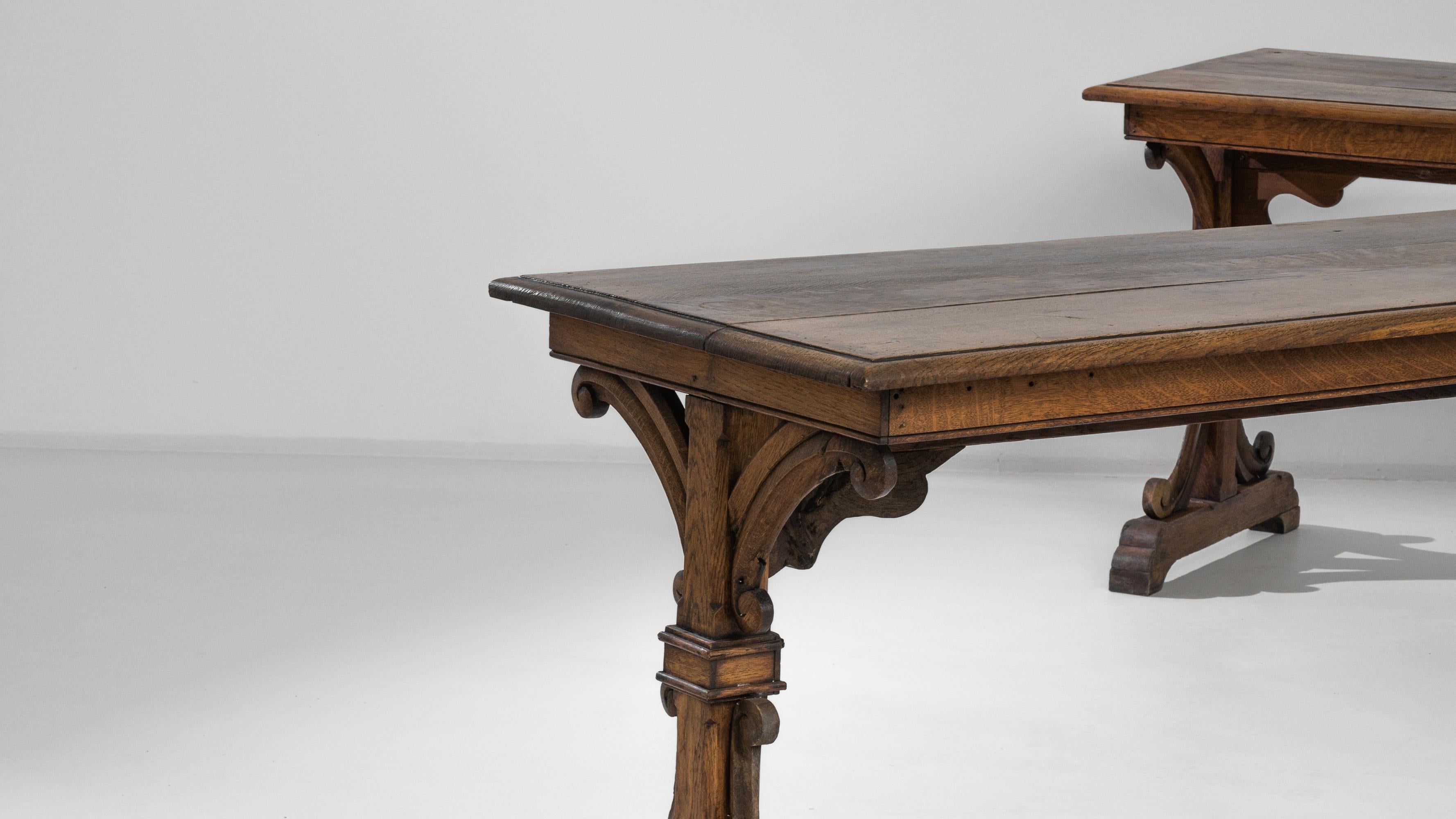 This beautiful pair of vintage wooden tables create a distinguished accent. Made by French furniture makers at the turn of the 20th Century. Carved scrolls bring embellishment and equilibrium to the trestle frame, while the rich hue of the original