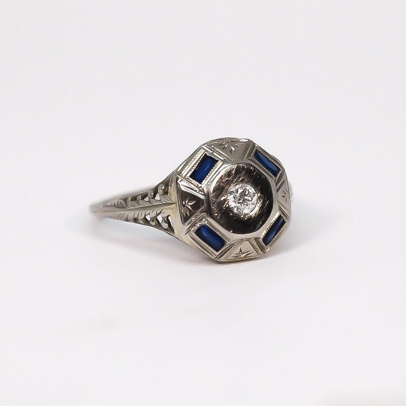 Beautiful vintage estate ring features octagon shape setting set with an antique round diamond and four baguette/scissor cut blue sapphires. The ring is engraved and cut out with a thin shank. The sapphires are natural medium blue, very even color.