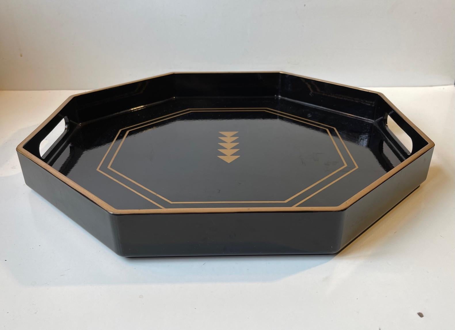 Wooden octagonal serving tray in black lacquer decorated with gold paint to the edges and the geometric centermotif. It was made in Japan during the 1960 or 70s. Measurements: W: 37.5 cm, H: 4.5 cm.
