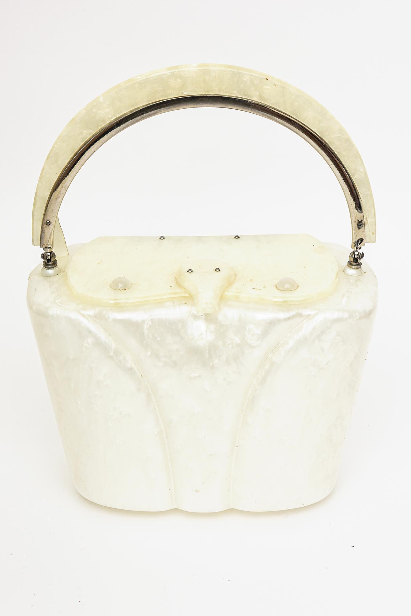 Ce très chic sac à main vintage des années 1950 est en lucite perlée blanc cassé et a été réalisé par la société Llewellyn de New York.
Il est noté comme tel sur la charnière. La poignée et d'autres parties sont cerclées d'un métal argenté. Il