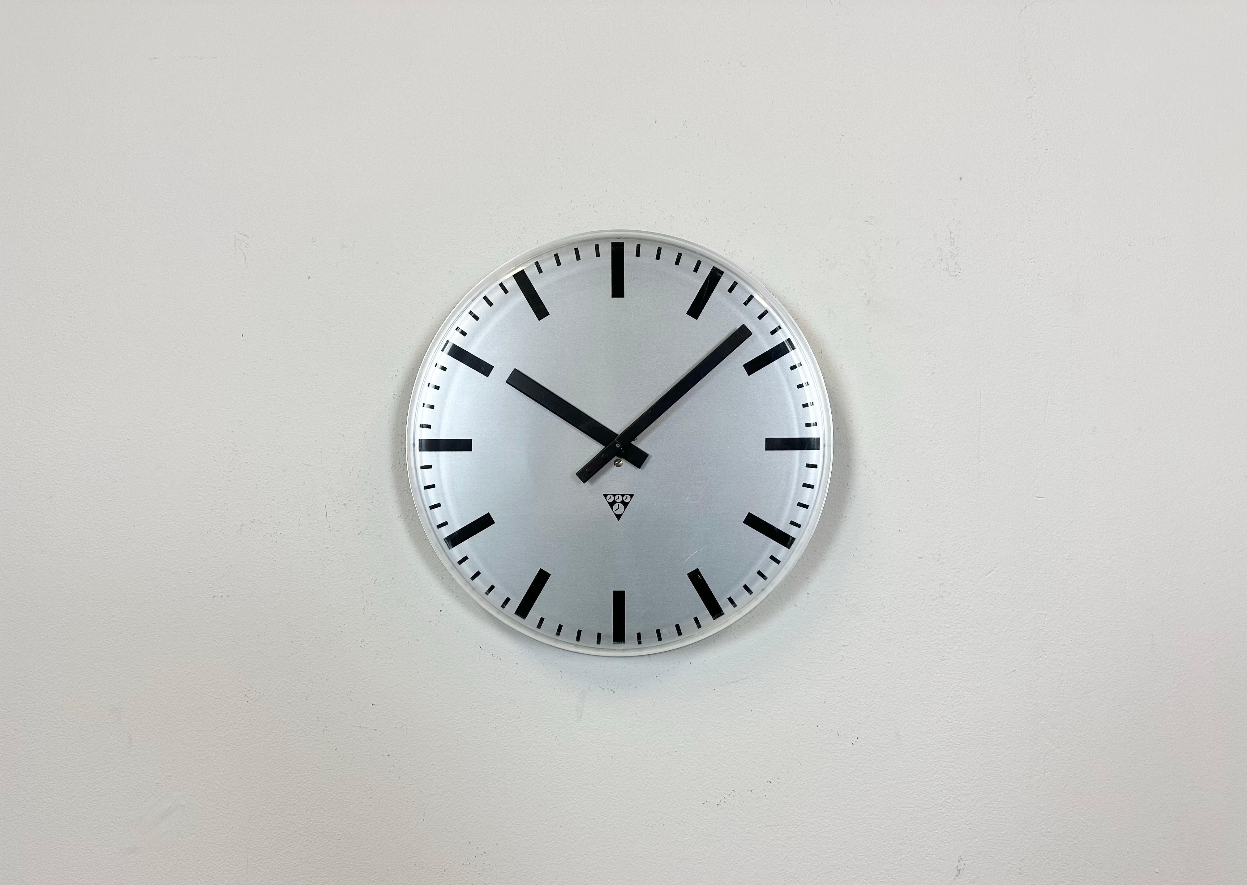 Cette horloge murale industrielle a été produite par Pragotron dans l'ancienne Tchécoslovaquie dans les années 1980. Il est doté d'un cadran en aluminium gris et d'un couvercle en verre transparent en plastique incurvé. La pièce a été convertie en