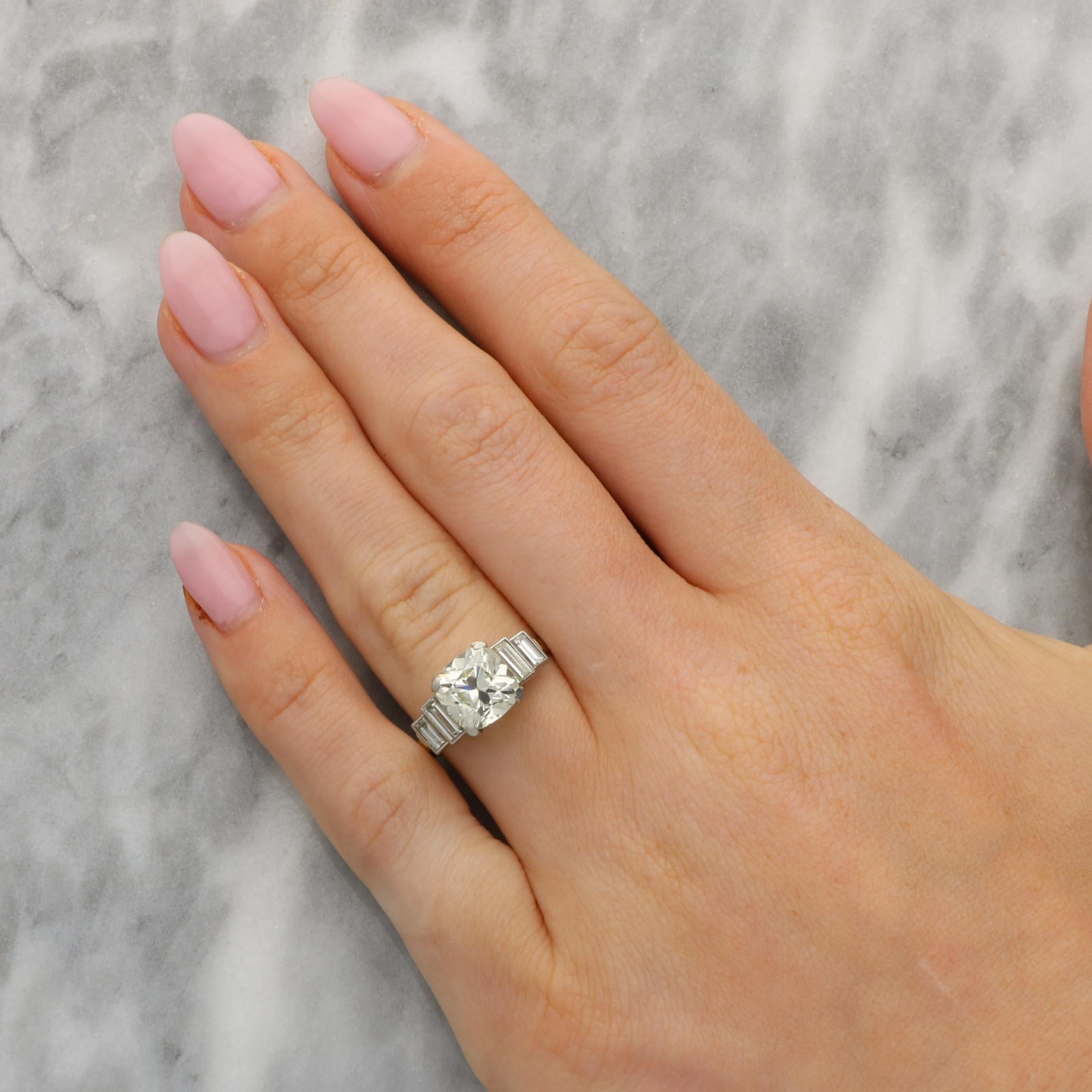 Une étincelante bague vintage ancienne en or blanc 18k, ornée de diamants de taille coussin et de diamants de taille baguette. 

La pièce est sertie au centre d'un magnifique diamant ancien de 2,50 carats de taille coussin, qui est solidement serti