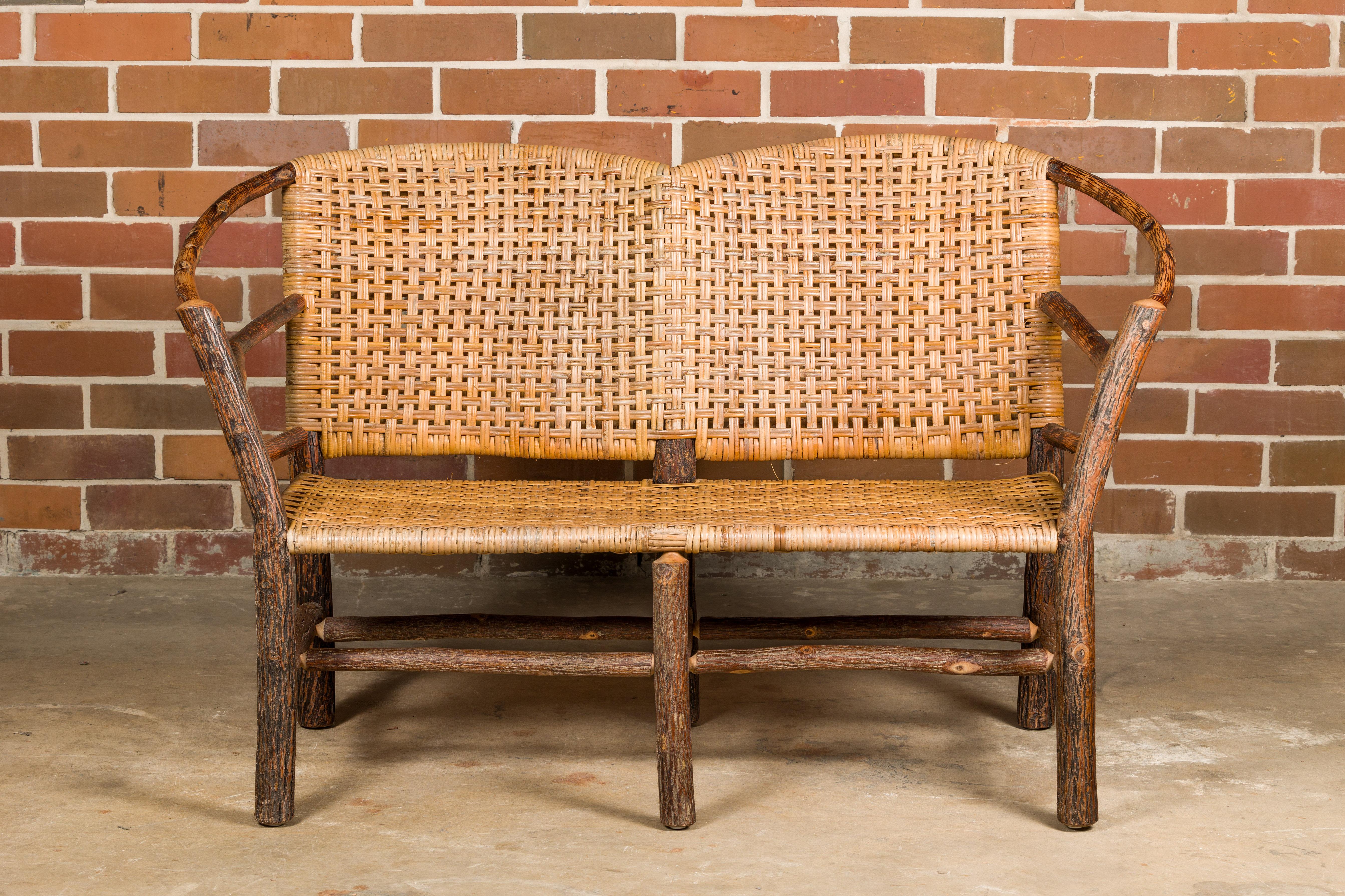 An Old Hickory hoop settee from the mid 20th century with woven rattan back and seat. This mid-20th-century Old Hickory hoop settee is a rustic masterpiece that seamlessly blends natural elements with functional design. Crafted with an artistic