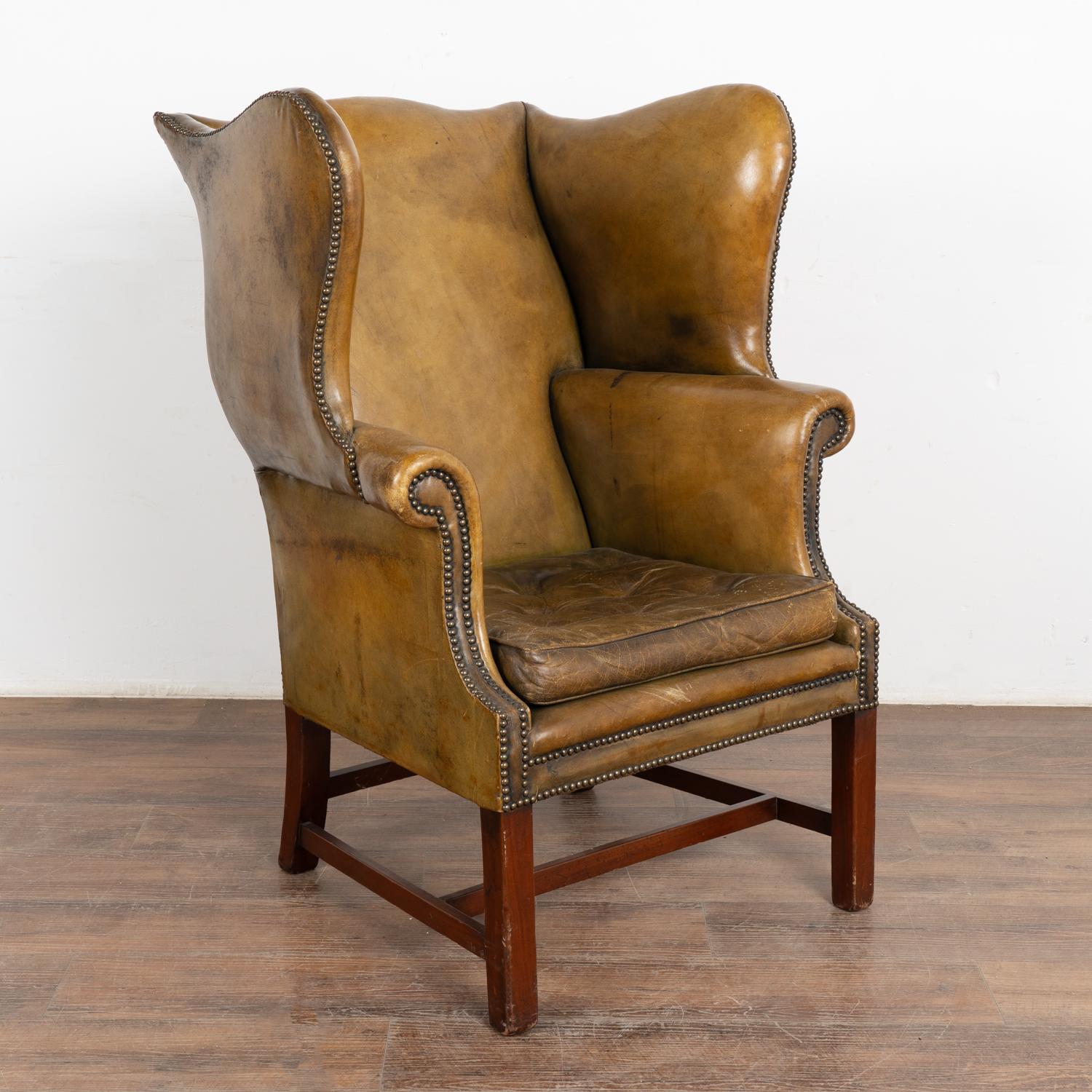 Vintage olive green leather George III style wingback arm chair with classic nail head trim, rolled arms and dramatic high back.
Sold in vintage used condition. Frame is solid/stable and sits comfortably; mahogany legs. Seat shows definite