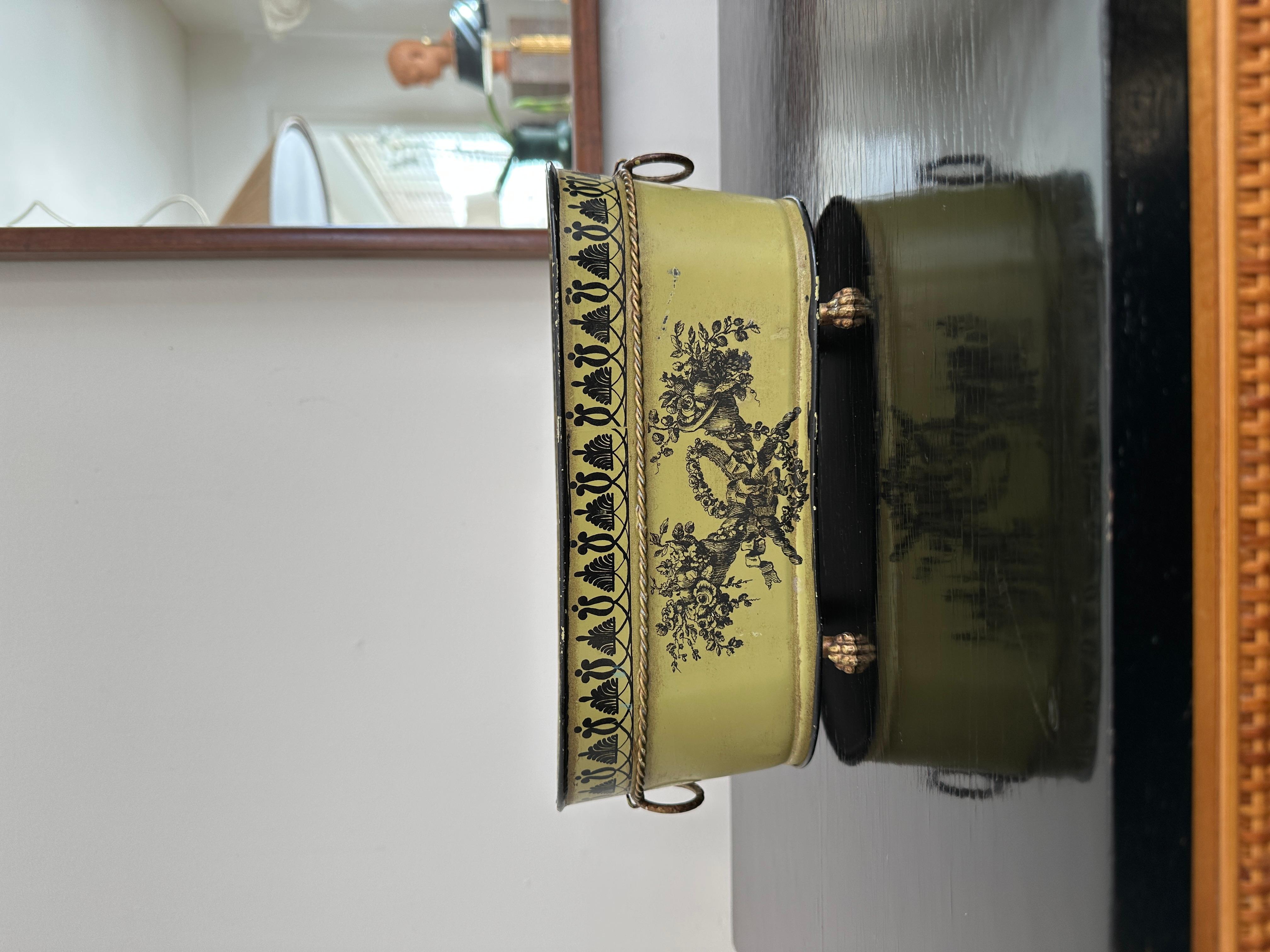 Una fioriera vintage in latta e toleware, di colore verde oliva, nero e oro, con stencil dorati, poggiata su zampe di leone e manici ad anello. Bellissimo modello reggenza con bordo a foglie d'acanto e cornucopie dorate, probabilmente realizzato