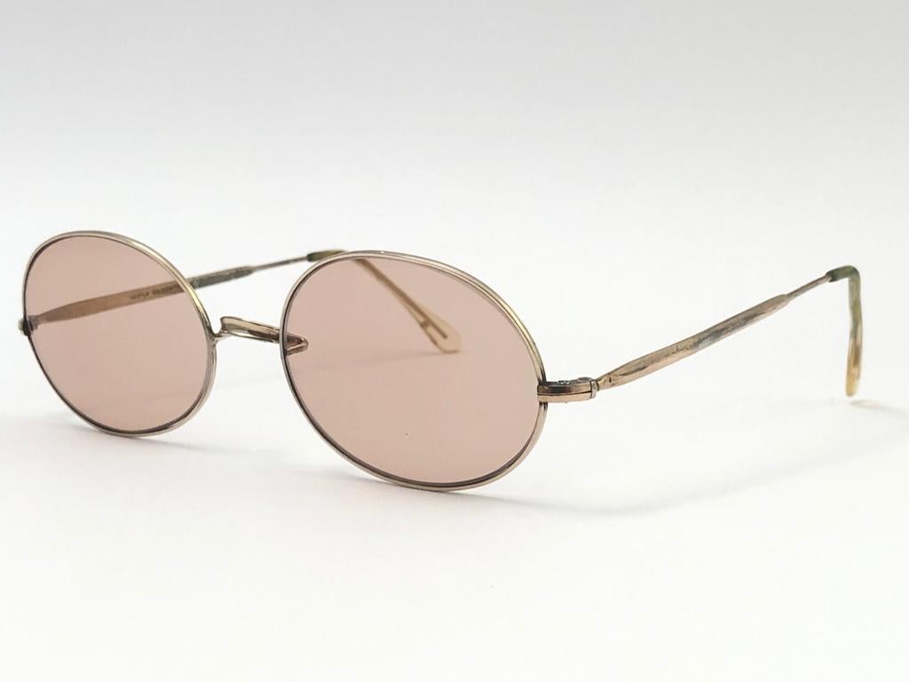 Rare paire de lunettes de soleil Oliver Goldsmith fabriquée au milieu des années 60, le même modèle que celui porté par Sharon TATE.
Délicate monture ovale dorée contenant une paire de lentilles marron clair. 

Cette paire présente des signes