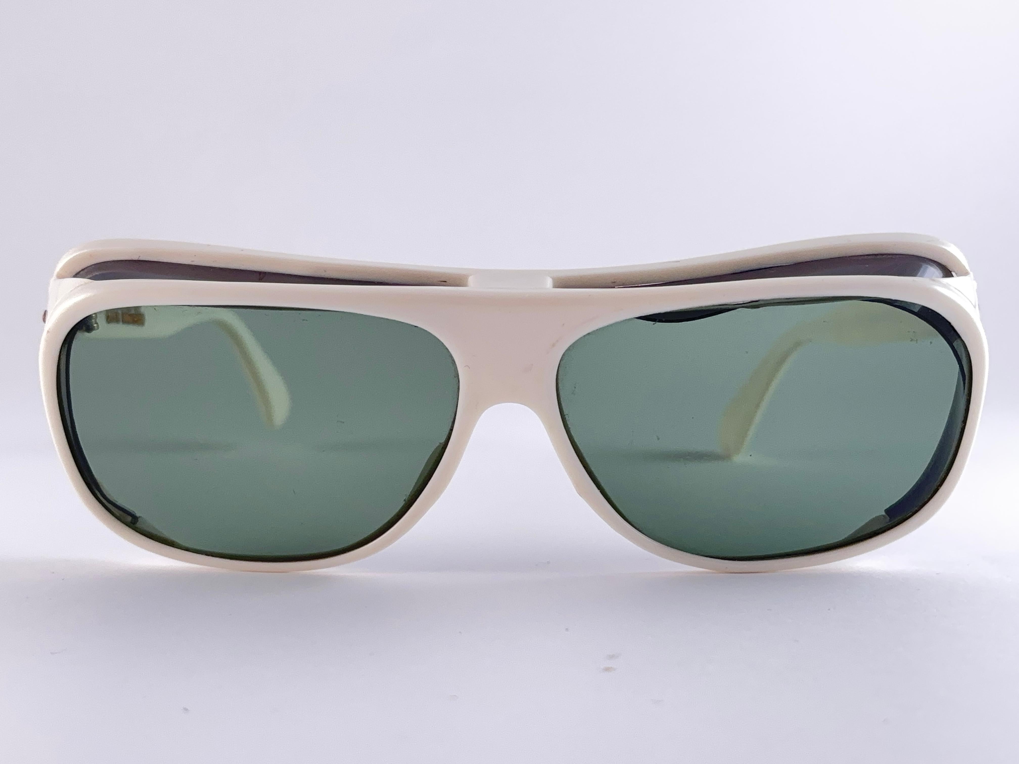 Oliver Goldsmith Sonnenbrille in Übergröße. 

Übergroßer weißer Rahmen mit seitlichen und oberen Aussparungen, der ein Paar mittelgraue Gläser hält. 

Dieses Paar zeigt sichtbare Anzeichen von Verschleiß durch die Lagerung.

Handgefertigt in