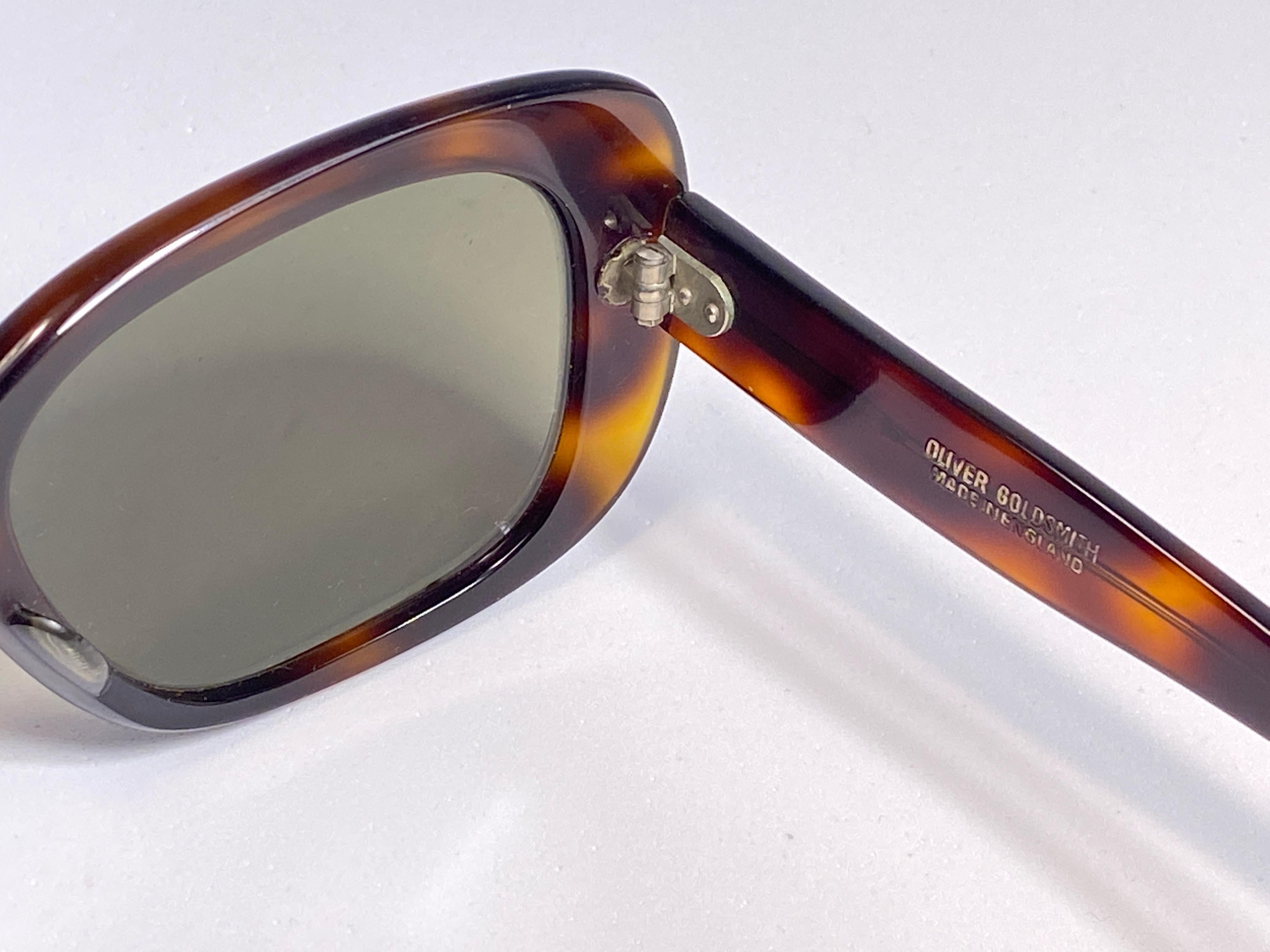 Paire robuste de lunettes de soleil Oliver Goldsmith. Monture tortue surdimensionnée contenant une paire de verres vert foncé.   

 Cette paire présente des signes mineurs d'usure.

Fabriqué à la main en Angleterre.