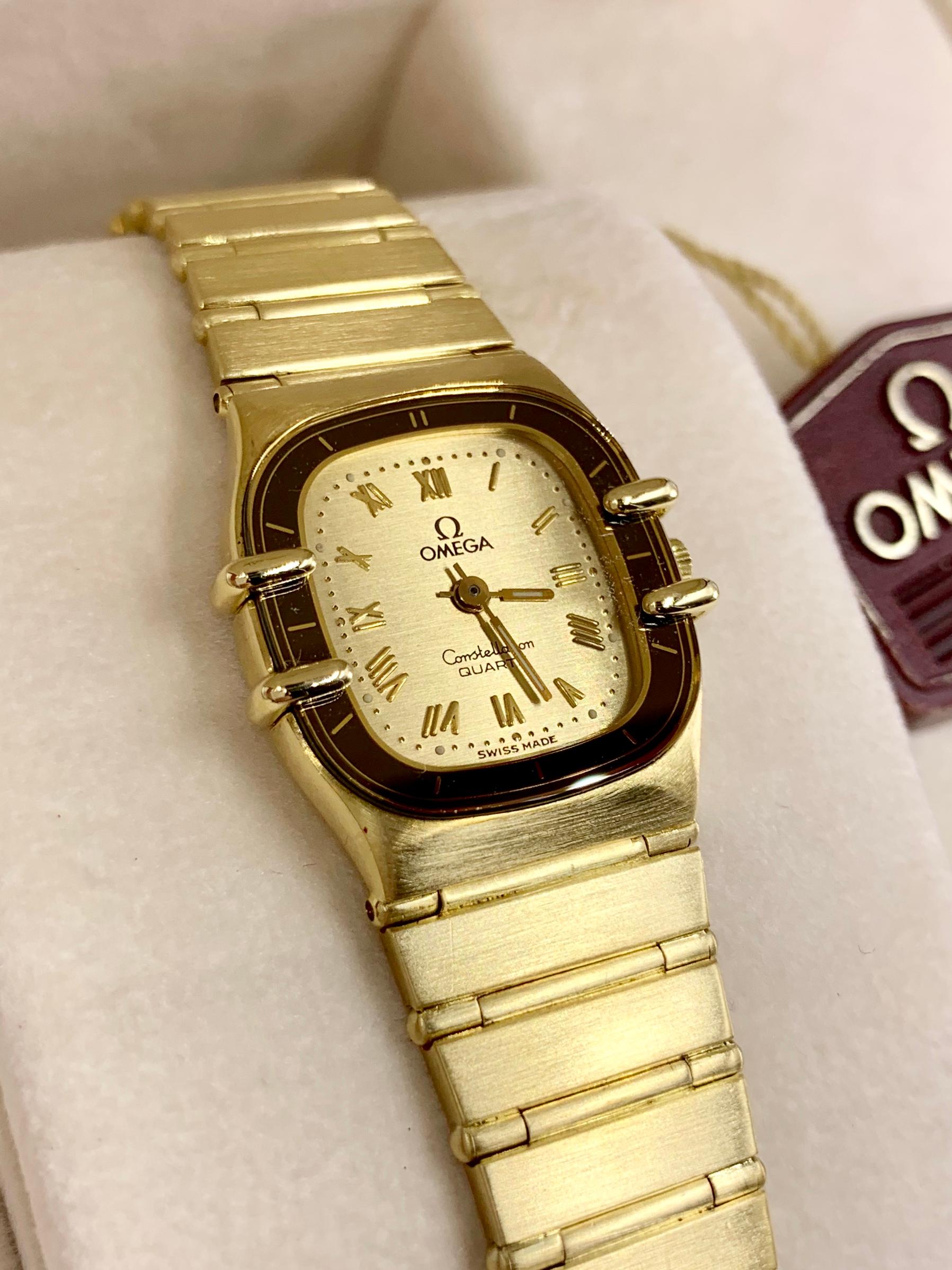 A wearable and chic all satin finished 18 karat yellow gold vintage Omega quartz timepiece from the iconic Constellation collection on the Manhattan bracelet. The cushion shaped case has a champagne satin dial with polished roman numerals and a