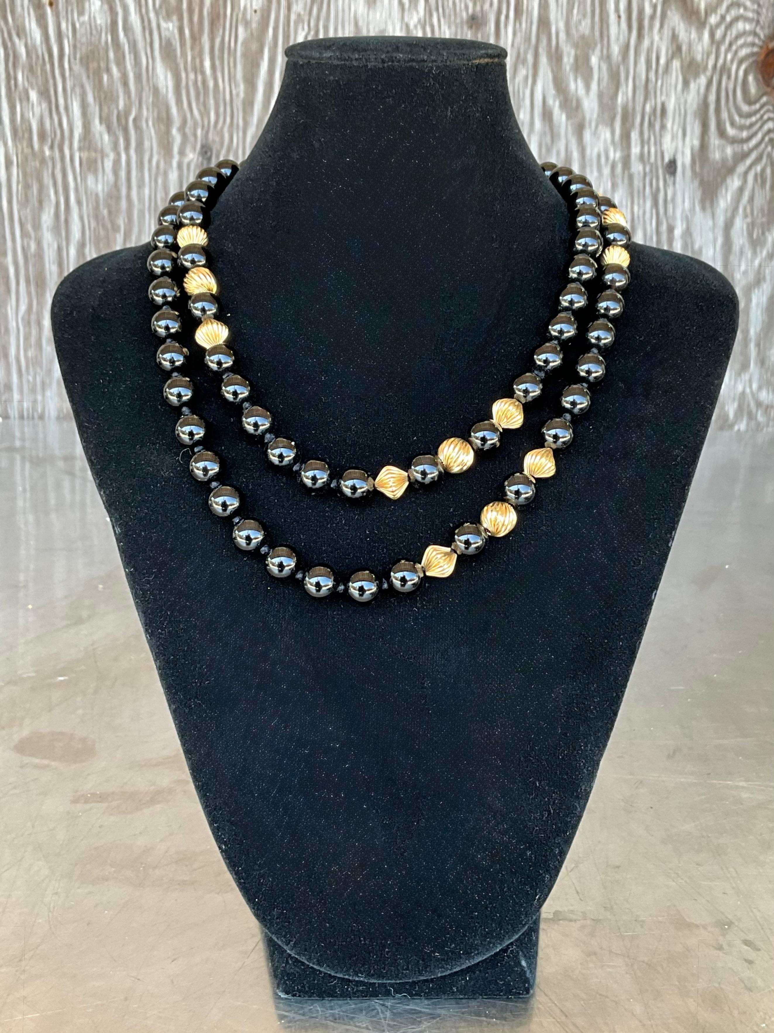Este impresionante collar vintage es una pieza atrevida y elegante, con cuentas de ónice pulido combinadas con elementos de oro de 14 quilates ricamente embellecidos. Cada gruesa cuenta se selecciona cuidadosamente por su intenso brillo negro, que