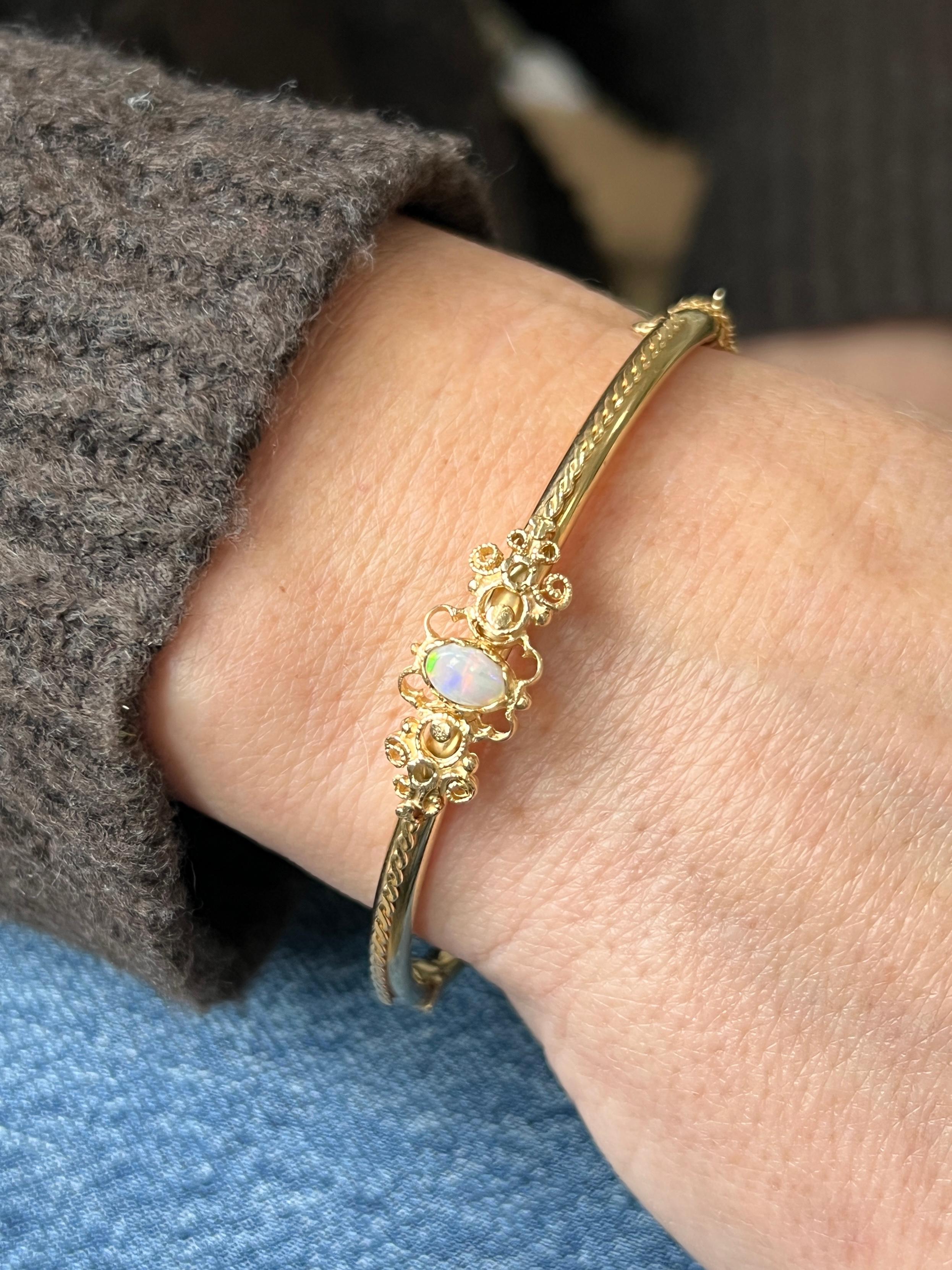 Questo braccialetto vintage degli anni '60 in oro giallo 14 carati presenta un elegante design in filigrana centrato da un singolo opale ovale di circa 5,98 x 3,88 mm. L'opale mostra giochi di colore morbidi e luminosi che si integrano con i caldi