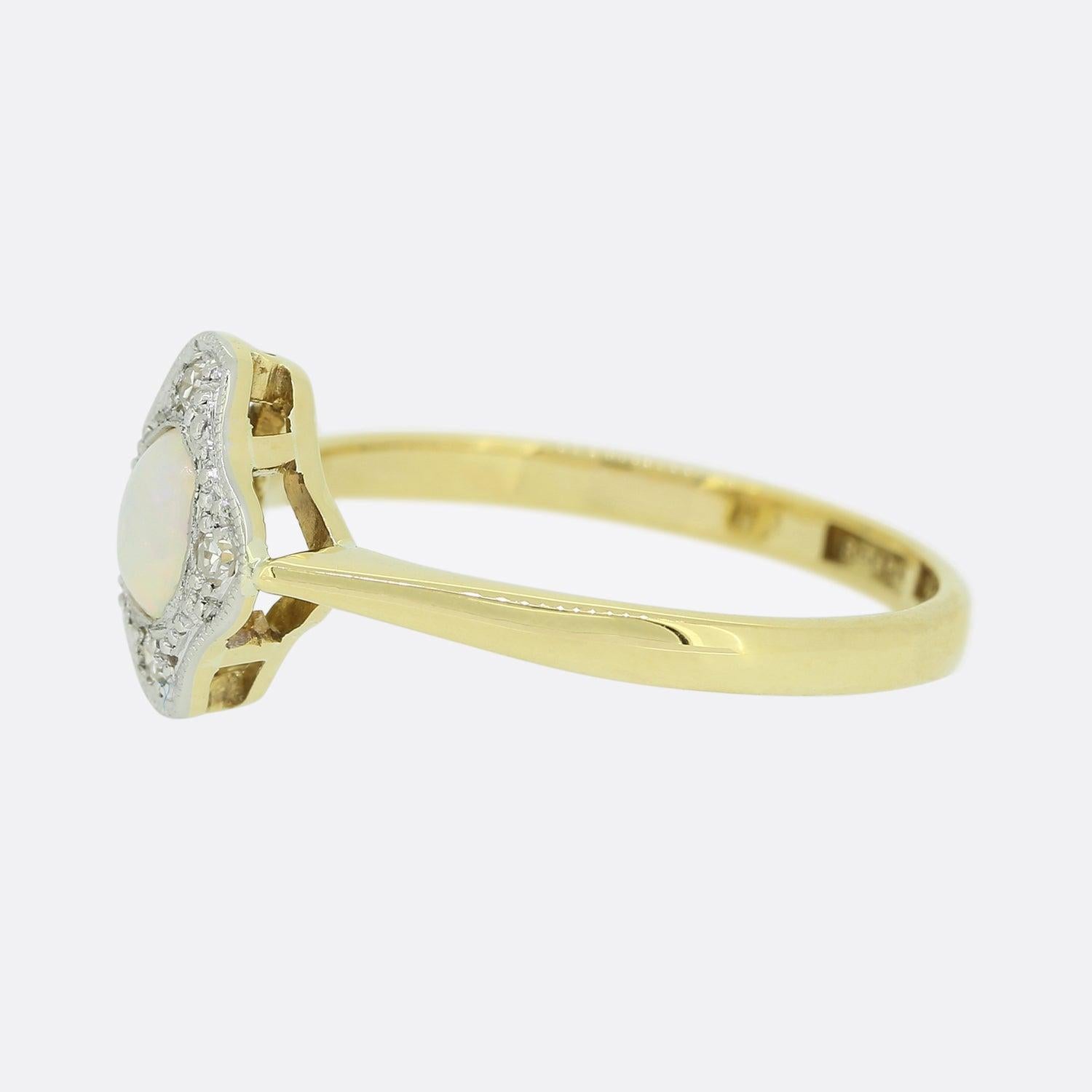 This is an 18ct yellow gold opal and diamond ring. The centralised white opal possesses a lovely iridescent play of colour and is set in the middle of four single cut diamonds. Each stone here is set in platinum and contained within a milgrain frame