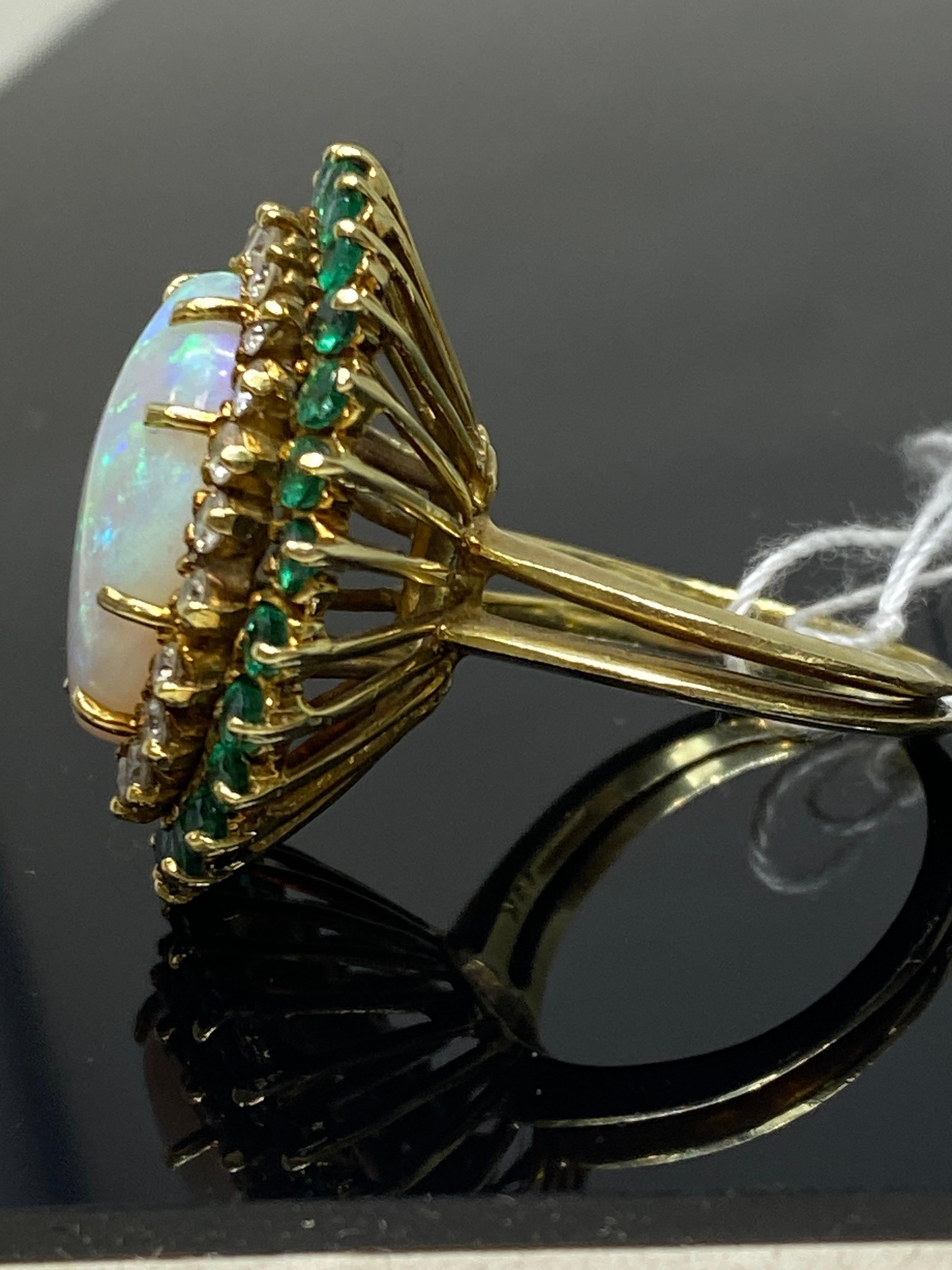 We instantly fell in love with showstopper of a ring as soon as we saw it.  It features a large vibrant 7 carat opal at the center surrounded by a double halo of sparking natural near colorless diamonds and natural green emeralds. Crafted in 18