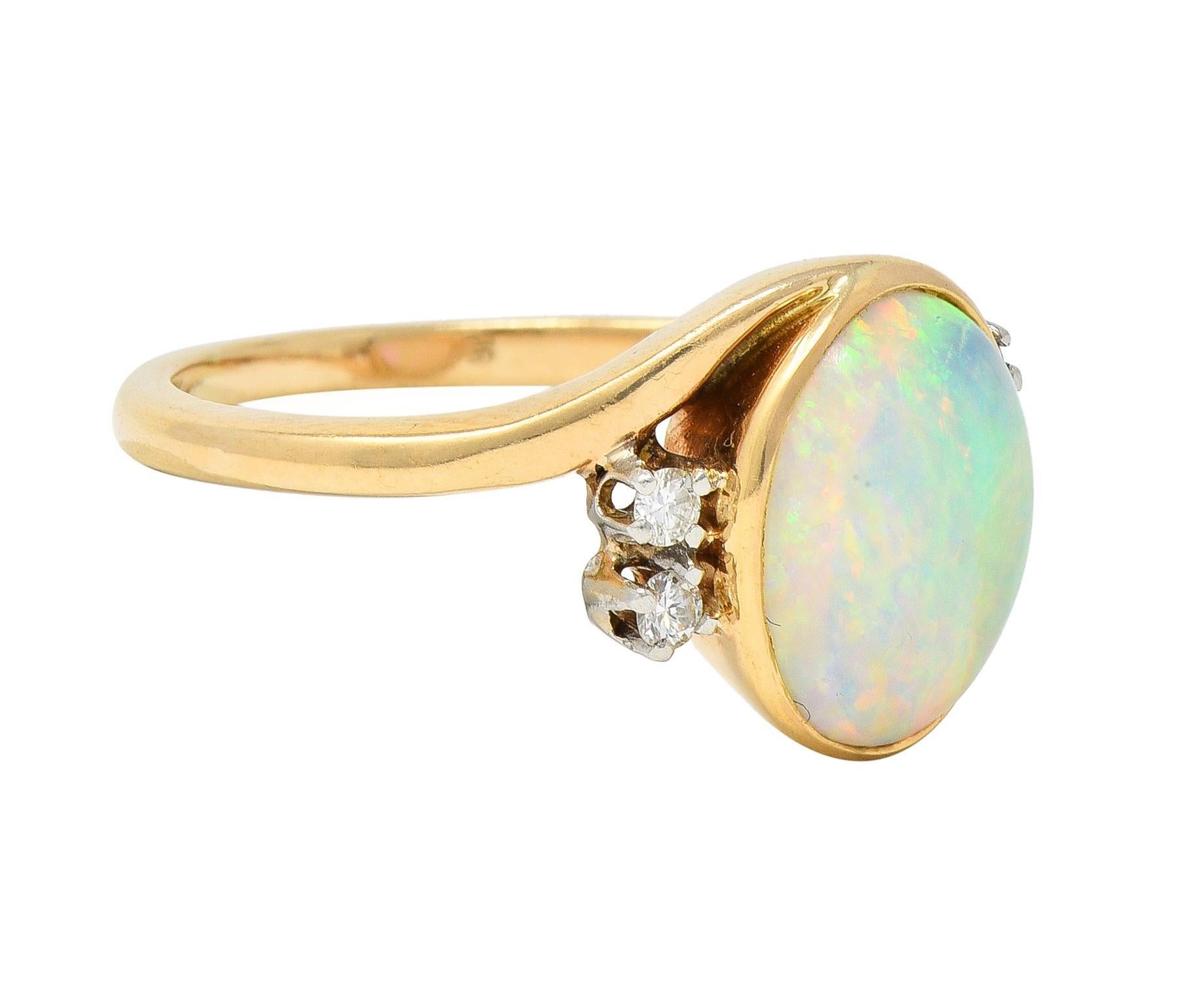 Centering a bezel set oval-shaped opal cabochon measuring 9.0 x 11.0 mm 
Translucent white in body color with strong spectral play-of-color 
Accented prong set round brilliant cut diamonds
Prong-set in platinum - weighing approximately 0.12 carat
