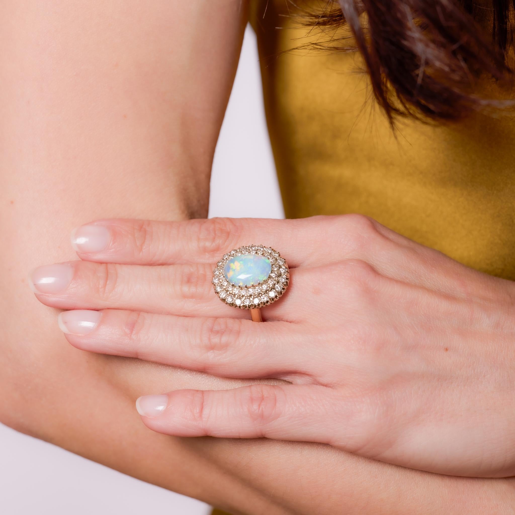 Crafted in the 1980s, this vintage cocktail ring features a captivating cabochon cut opal weighing approximately 2.15 carats, radiating with soft iridescence. Surrounding the opal are 42 round brilliant cut diamonds totaling approximately 1.30