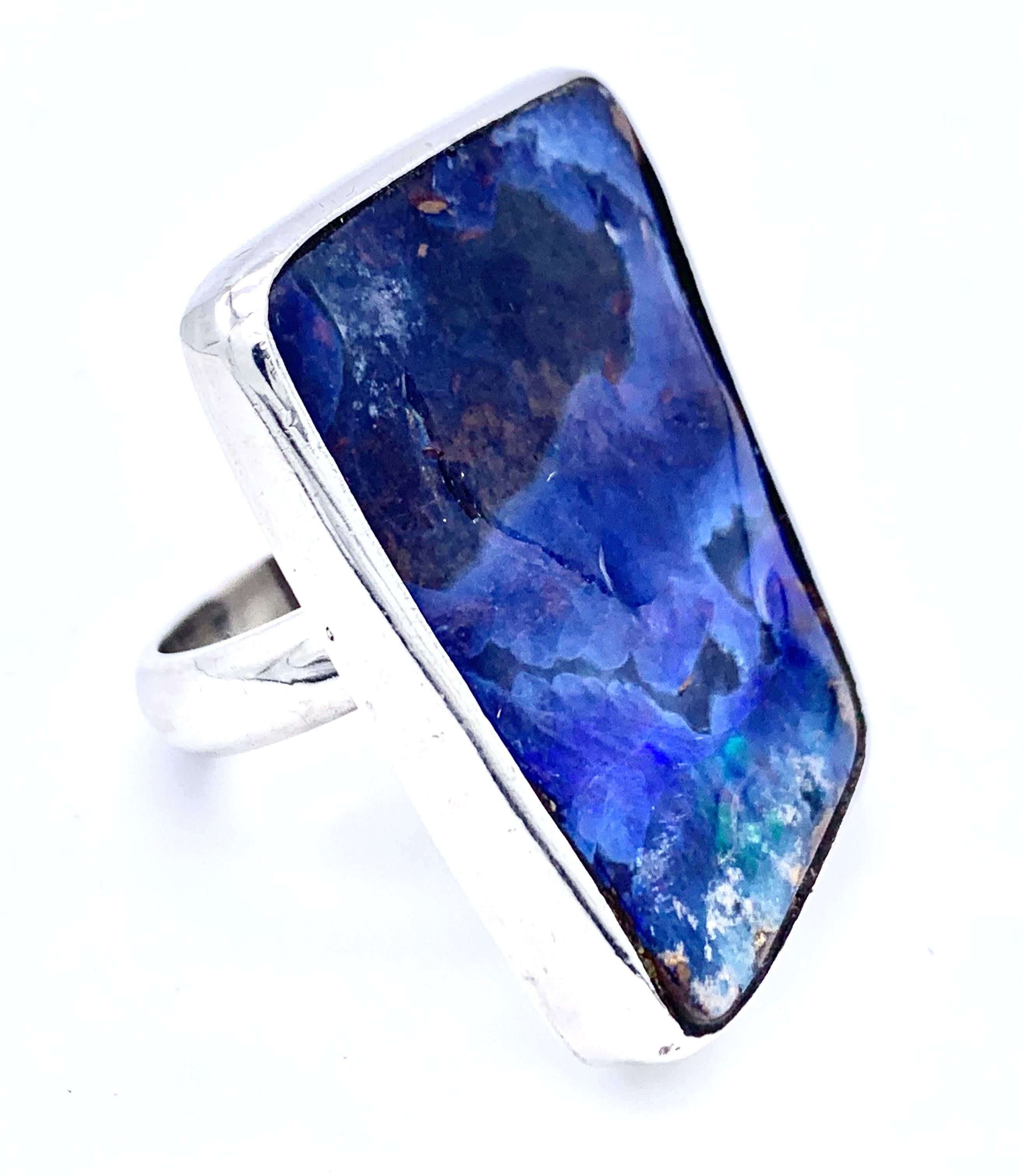 This large opal matrix ring is set in a sterling silver mount, The asymmetrical slice shows a wonderful array of blues and some fluorescent red specs. The stone has been polished to a flat, slightly concave surface which shows some natural