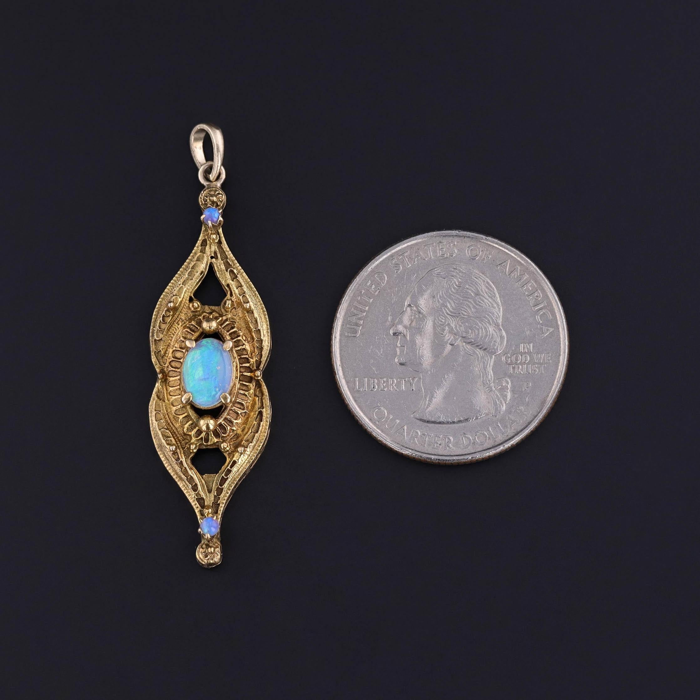 Questo ciondolo vintage presenta un'opale ovale di cristallo con un gioco di colori ipnotico, accentuato da due opali più piccoli che aggiungono un delicato tocco di lucentezza. Le pietre sono incastonate in caldo oro 14k e i loro bagliori