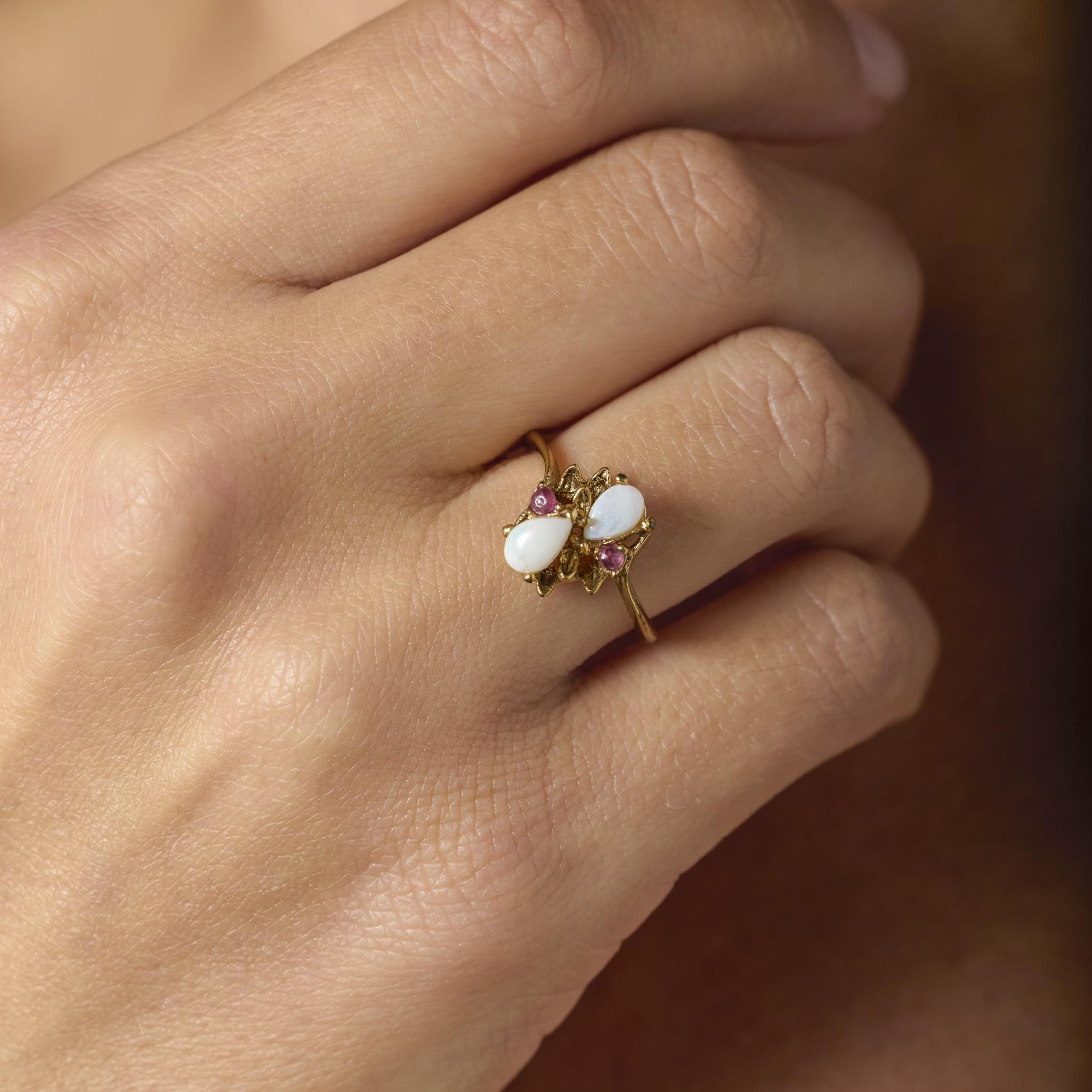 Cette charmante bague vintage en or jaune 14k présente deux opales brillantes en forme de poire accentuées par des rubis vifs, mêlant chaleur et couleur dans un élégant design des années 1970.