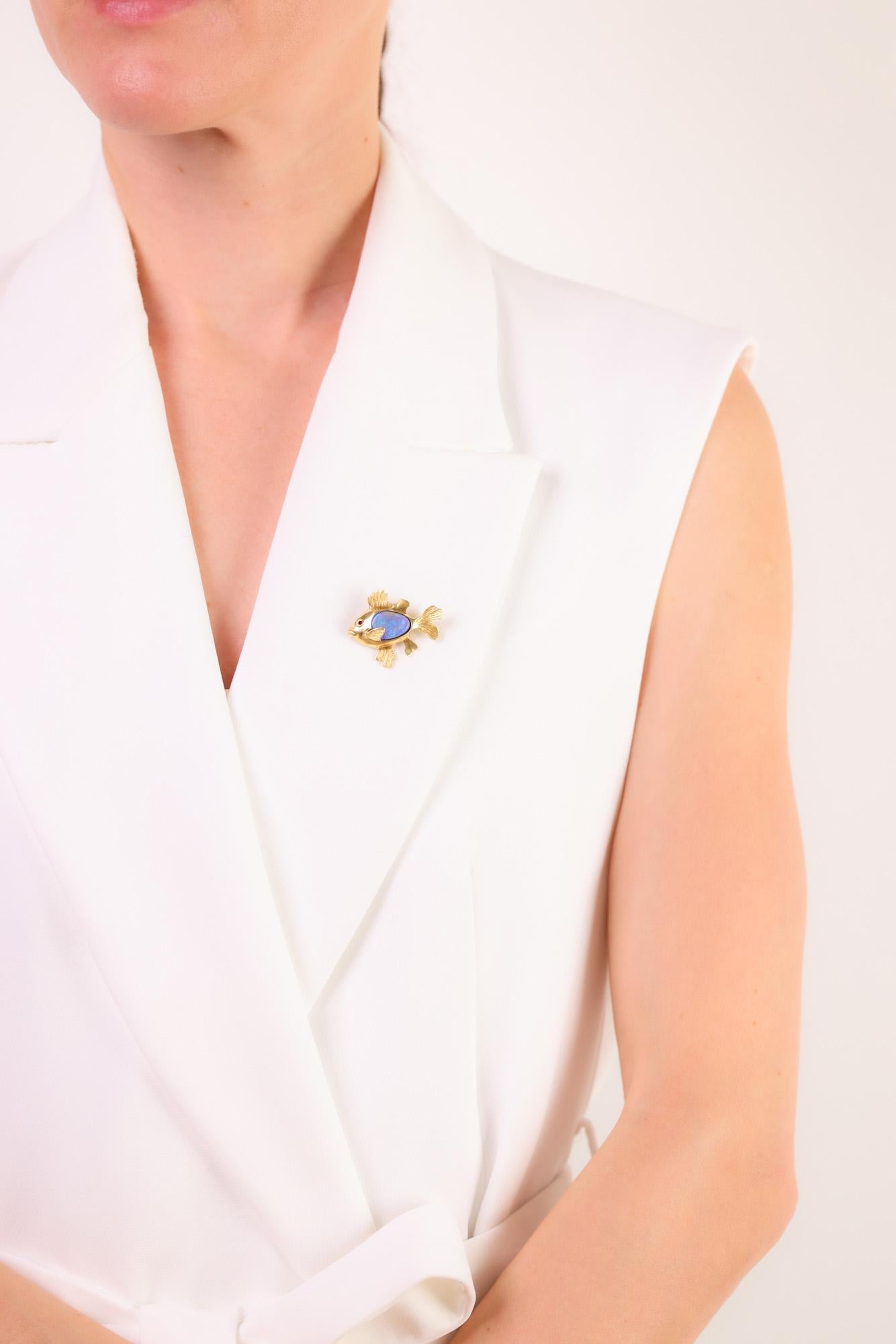 This vintage 1980s fish brooch features a luminous opal and a ruby accent, elegantly crafted in 18k yellow gold for whimsical charm.

Center stone: Opal
Accent stone: Round brilliant cut ruby
Weight: .01 carat
Metal: 18k yellow gold
Era: