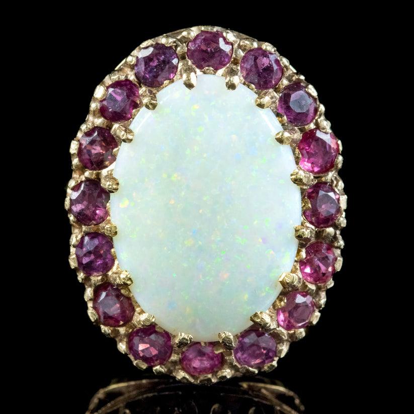 Ein extravaganter Cocktailring aus den 1970er Jahren mit einem großen Kristallopal in der Mitte, der ca. 14ct wiegt. Er schimmert in einem Regenbogen aus farbigen Sprenkeln und wird durch einen Heiligenschein aus sechzehn tiefrosa Rubinen von