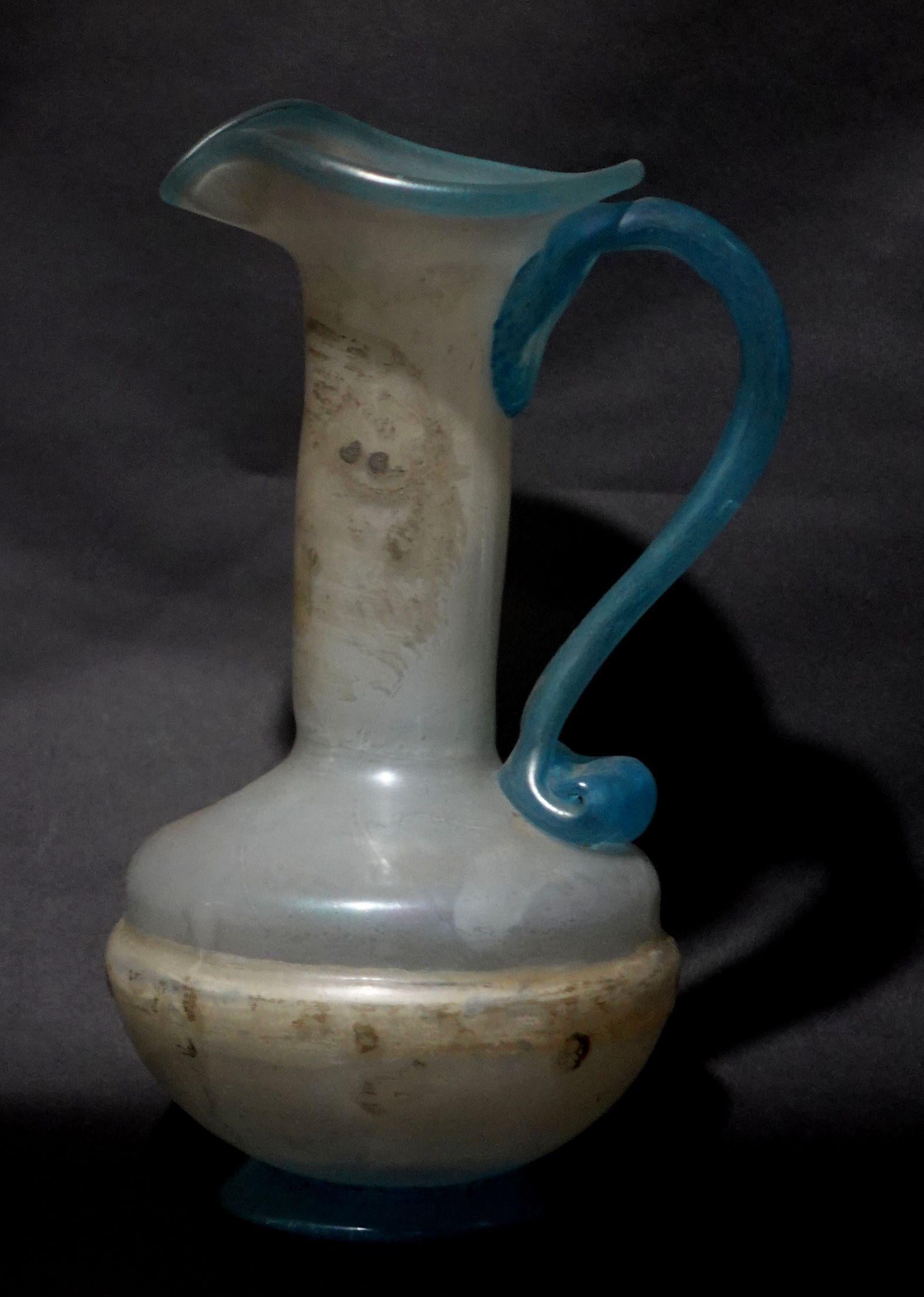 Bellissima brocca d'epoca in vetro artistico soffiato a mano e lavorato a mano in tonalità opache trasparenti e blu con pontili lucidati sul fondo. L'usura della superficie è coerente con l'esposizione. Misura circa 4,5 pollici di larghezza e 8,75