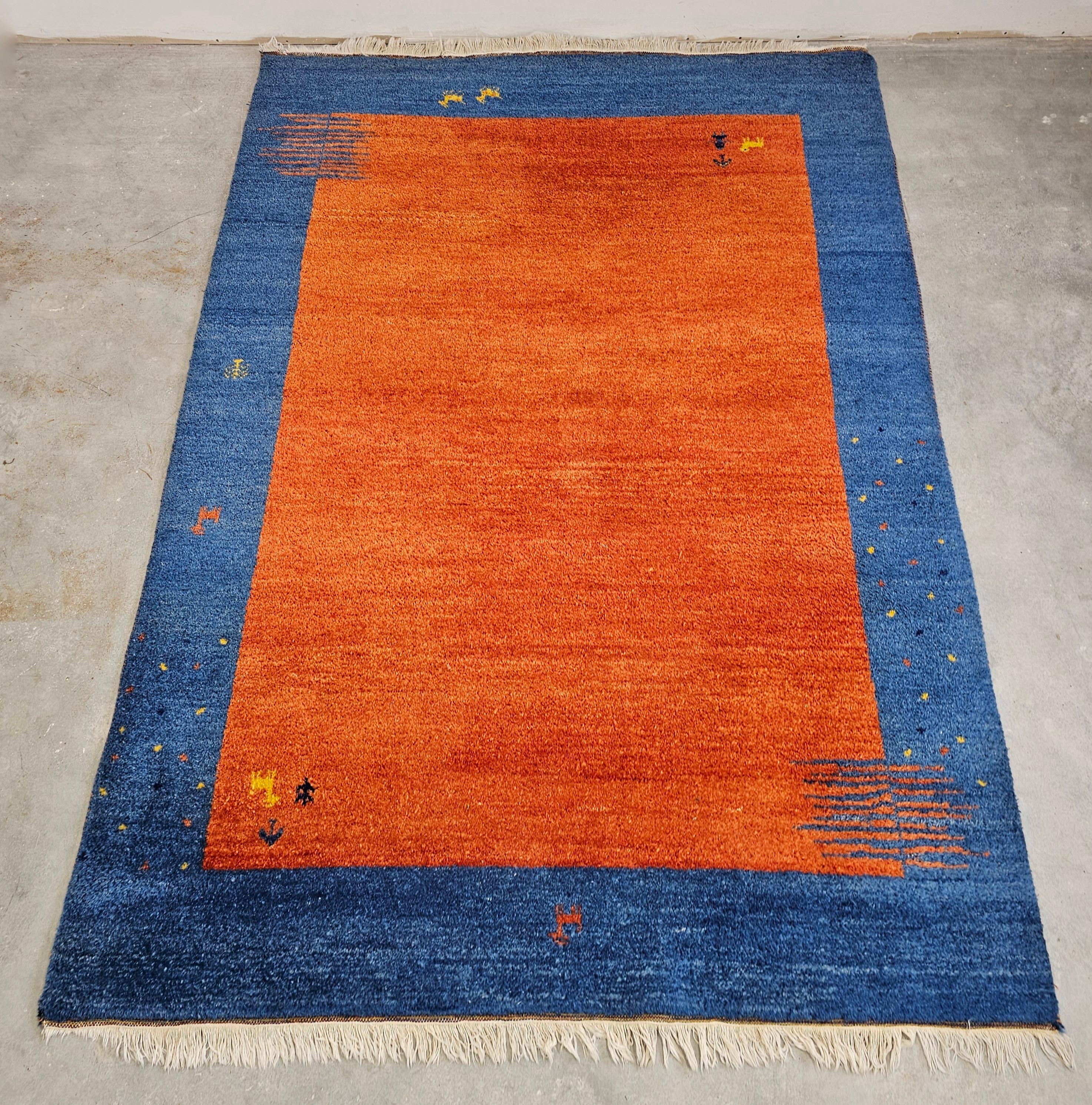 In this listing you will find an Orange and Blue Gabbeh rug, with very limited number of characteristic abstract patterns resembling animals and people. Its design combines two aesthetics that are not often combined - the Persian tribal aesthetics