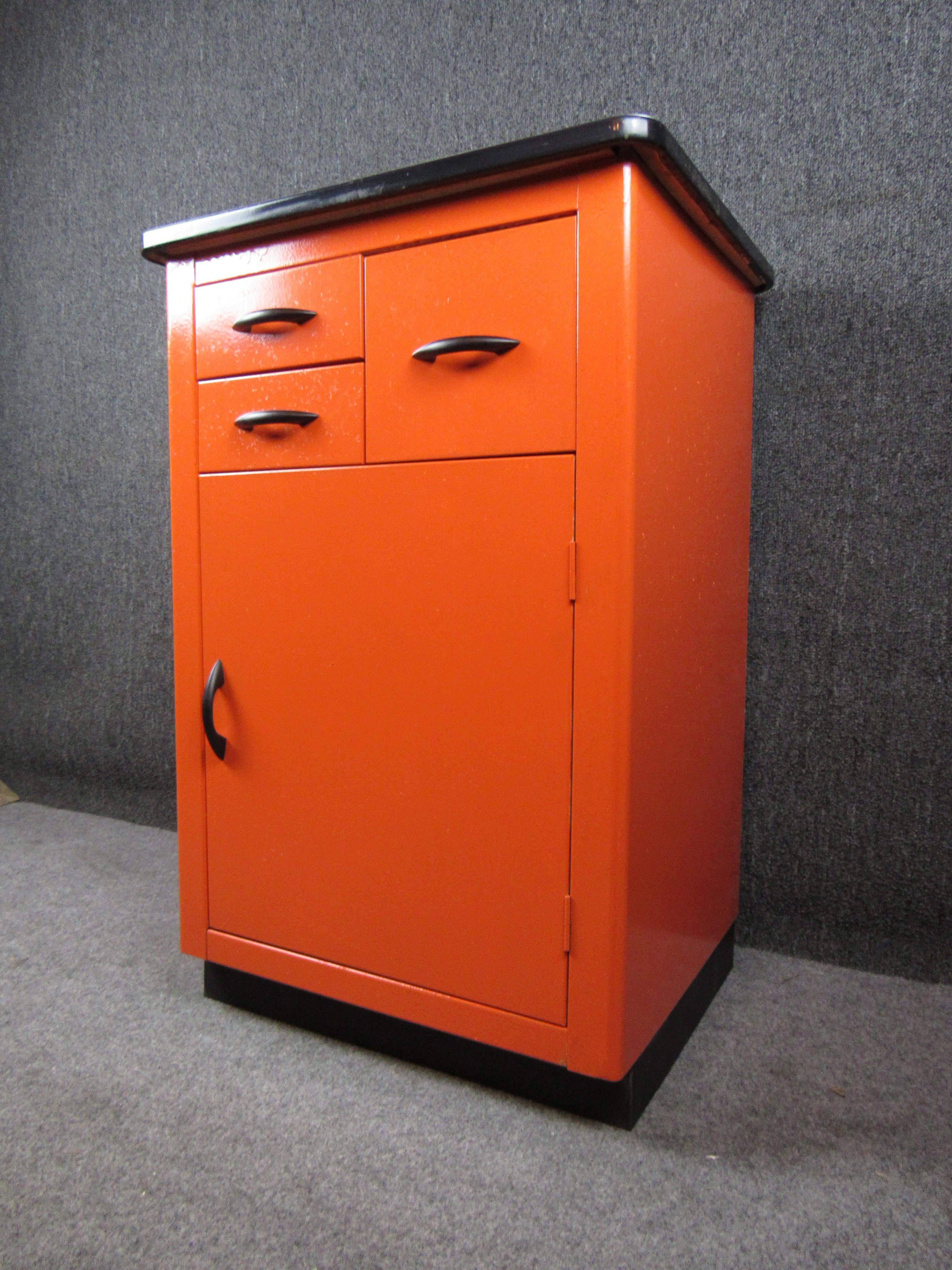 Bring home all the charm of a midcentury summer camp with this wonderful orange enameled metal cabinet. Featuring a clean white top and sharp black metal accents, this cabinet is sure to heighten the style of any room, whether in the home or office!