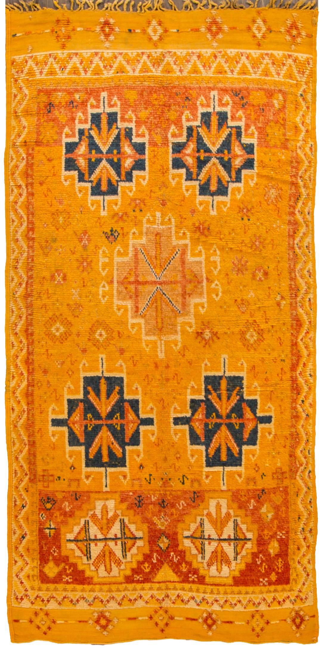 A hand-knotted vintage 1950s Moroccan rug with a geometric design on a yellow and orange field. Accents of red and dark blue throughout the piece. This rug measures 4.04x9