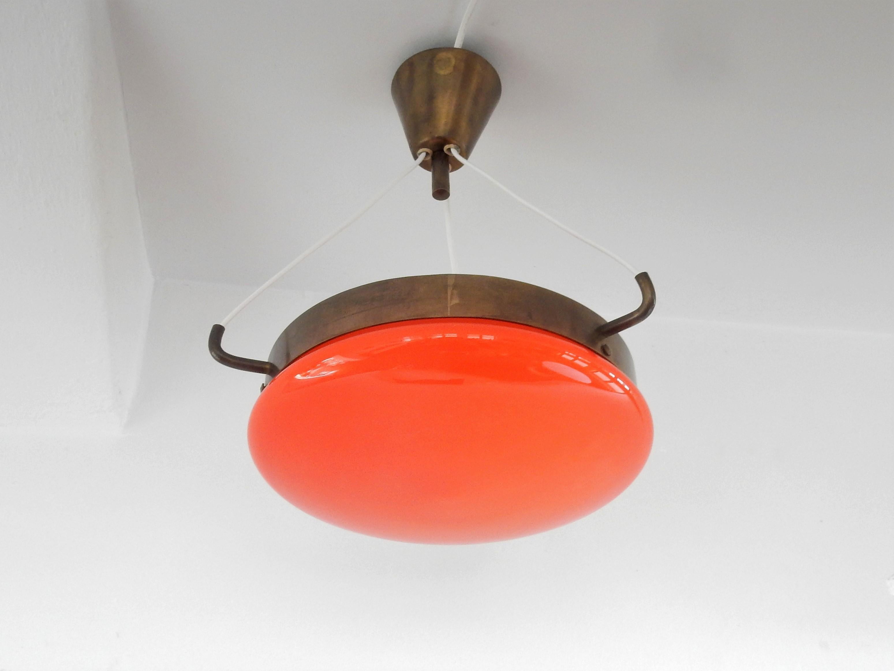 This elegant ceiling lamp is made of orange colored glass with a white inside and brass details. The glass is hung to the ceiling fixture by the brass ring with three attached wires. It gives a nice and warm light. The lamp is in a very good