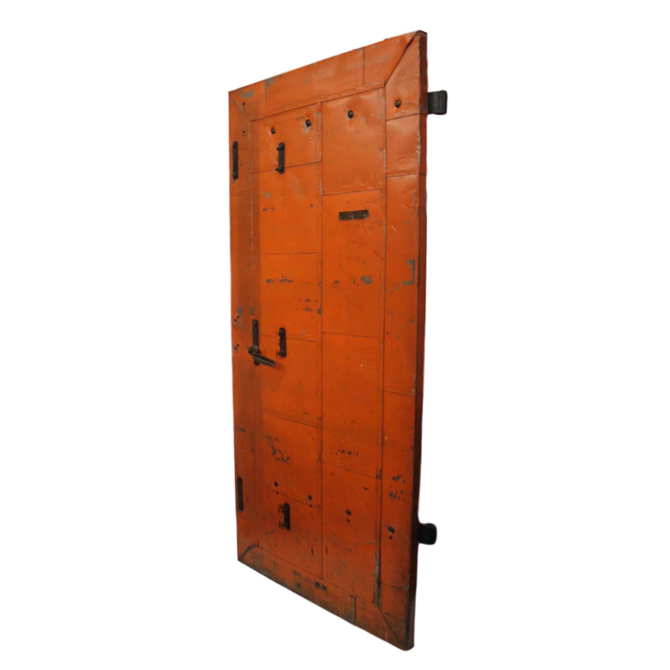 This heavy duty industrial fire door features a solid wood core completely sheathed in individual fire-proof steel-cladding, weathered orange paint and original hardware. Manufactured circa 1915 by The Richmond Fire Proof Door Co. of Richmond, IN.