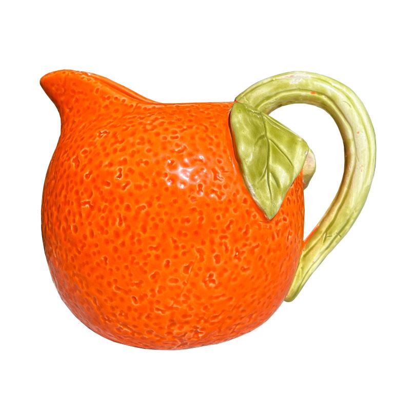A petite mid-century modern ceramic orange pitcher. This piece will be fabulous on a breakfast table. It is made of ceramic and resembles an orange fruit. The body is round with the texture of an orange peel. The handle is green and resembles the