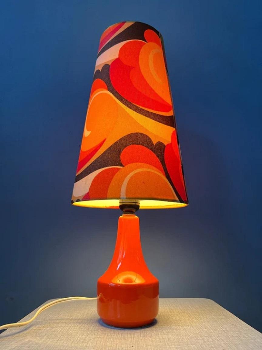A vintage space age table lamp with orange flower shade and ceramic base. The lamp requires one E27 lightbulb and currently has an EU-plug.

Dimensions: 
ø Shade: 21 cm
Height: 41 cm

Condition: Good. The shade has a slightly lighter colour on one