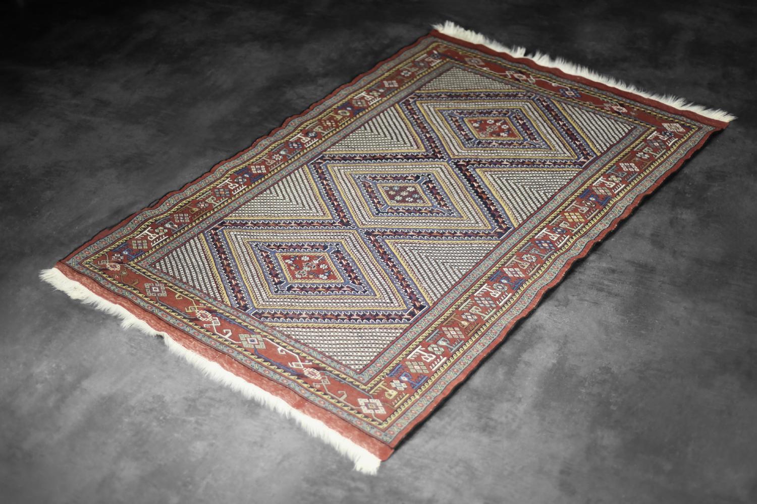 This hand-woven Shiraz rug was made in Iran during the 1960s. It is dyed in shades of red, navy blue, beige, and black with subtle accents of white and made of natural wool on a cotton warp. This rug is hand-woven by artisans from southwestern Iran,