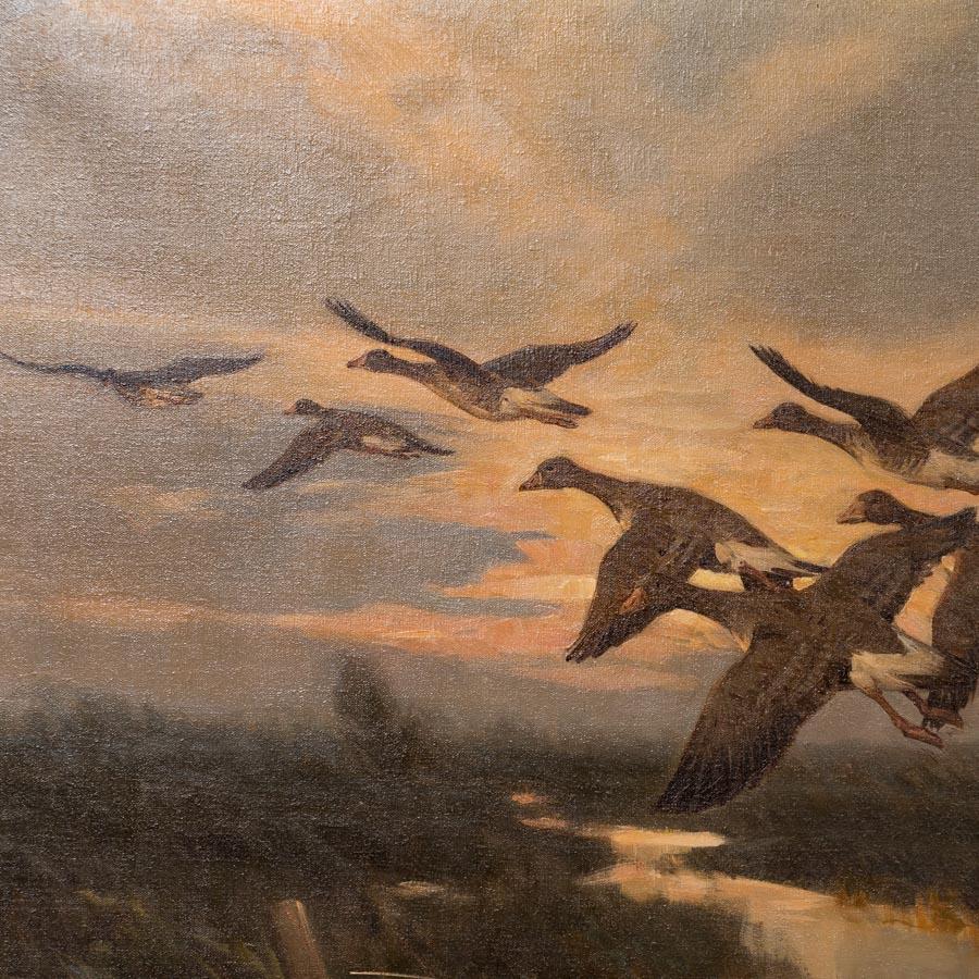 The exceptional detail and use of light evokes the sounds and feel of geese taking flight from a marsh in this original vintage painting. The flock flies through the rays of the rising sun, diffusing the light and highlighting the clouds above and