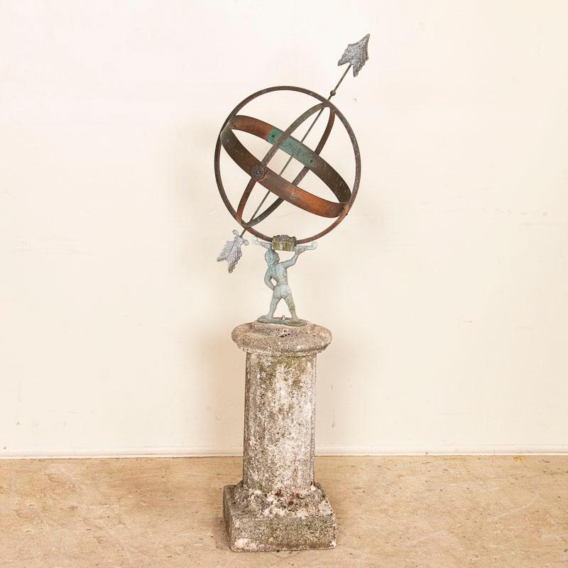 Antique garden ornament from Denmark, known as a Sun Clock or Armillary, with a cast metal figure holding spherical rings and mounted on a pedestal base (representing Atlas holding up the world). The metal of this sun dial has an aged verdigris