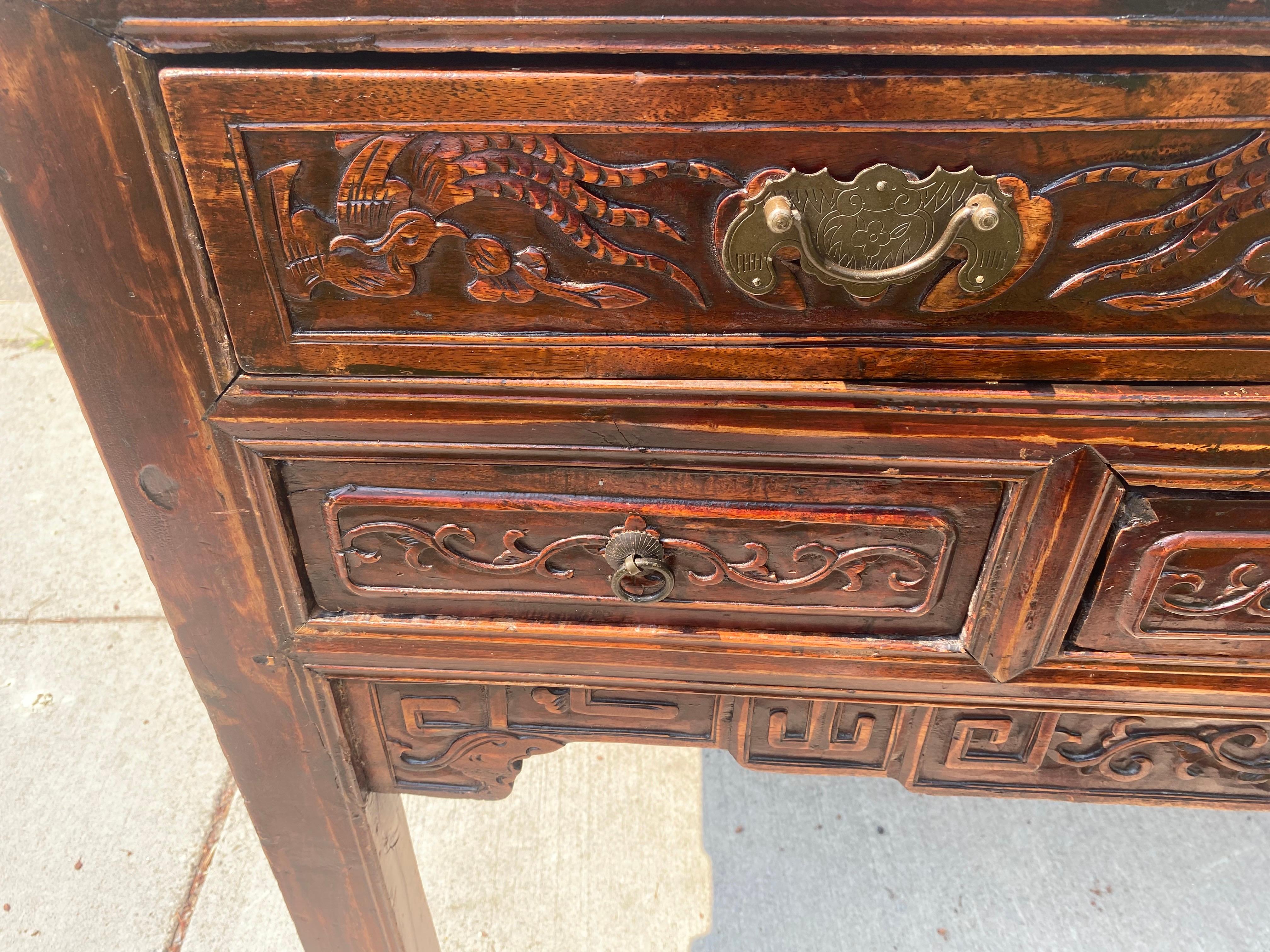 Se trata de una mesa auxiliar oriental de mediados del siglo XX tallada a mano. Esta mesa rústica tiene cinco cajones tallados a mano en la parte delantera y tallados en el faldón y los laterales. Esta pieza presenta los herrajes originales y fue