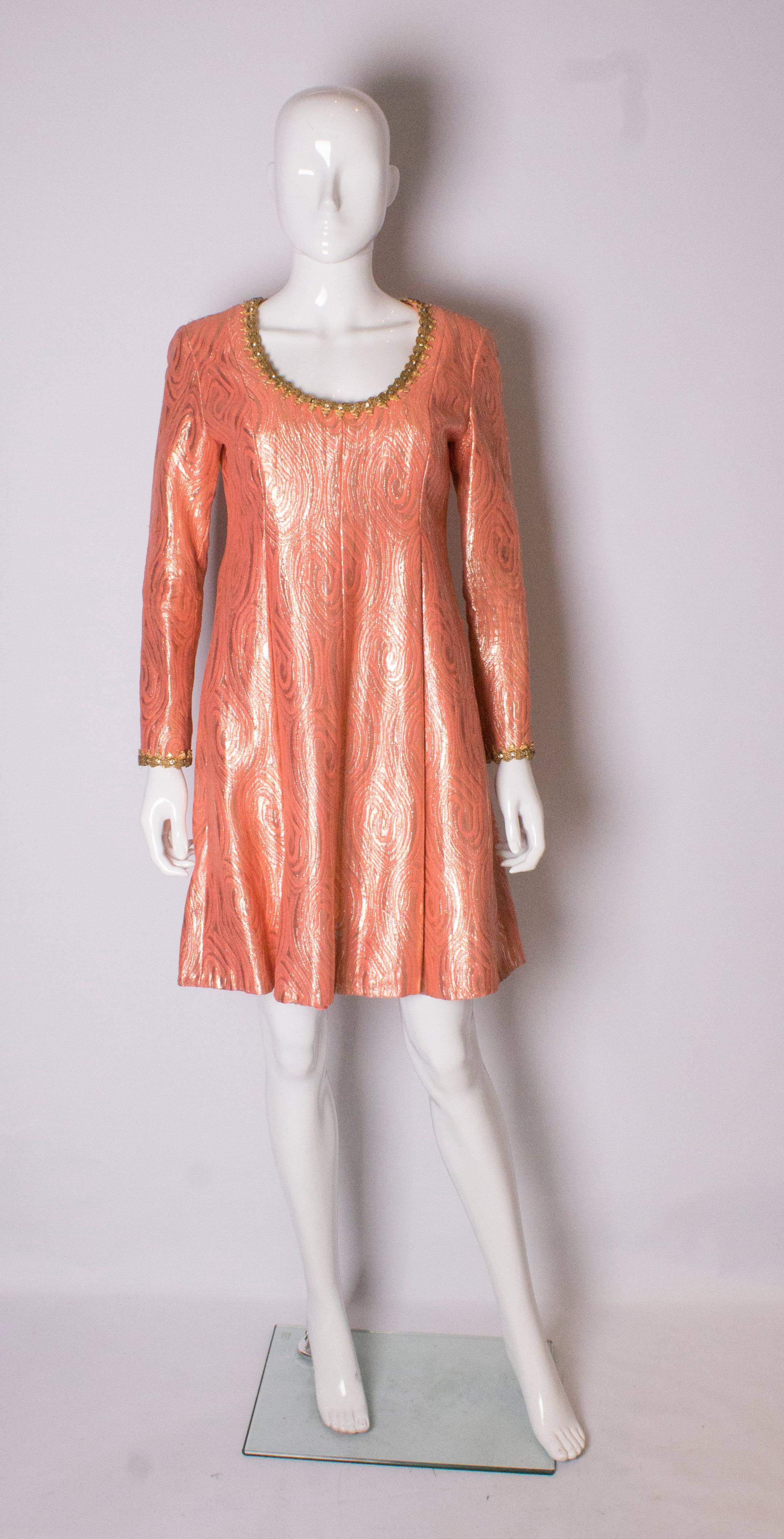 A great dress by  Oscar de la Renta. The dress is in a colourful combination of soft golds and tangerine with beautiful braiding on the neckline and cuffs. The dress has a scoop neckline, central back zip and is fully lined.  It has pleats at the