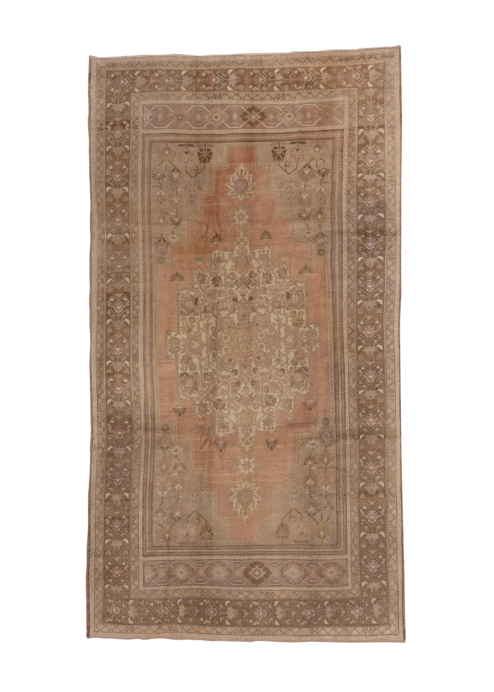 This west Anatolian city piece with a coarse weave, shows a rusty salmon open field hosting a large stepped ecru medallion with petal palmette pendants. At each field end is an extras panel (etek) with a doubly connected hexagonal repeat design.