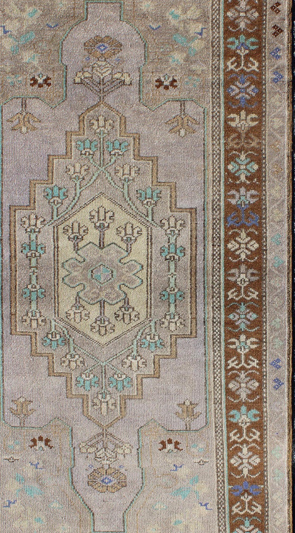 This vintage Turkish Oushak rug (circa mid-20th century) features a unique blend of colors. The multi-layered central medallion is complemented by a symmetrical set of floral motifs in the surrounding cornices and border. The various shades of Soft