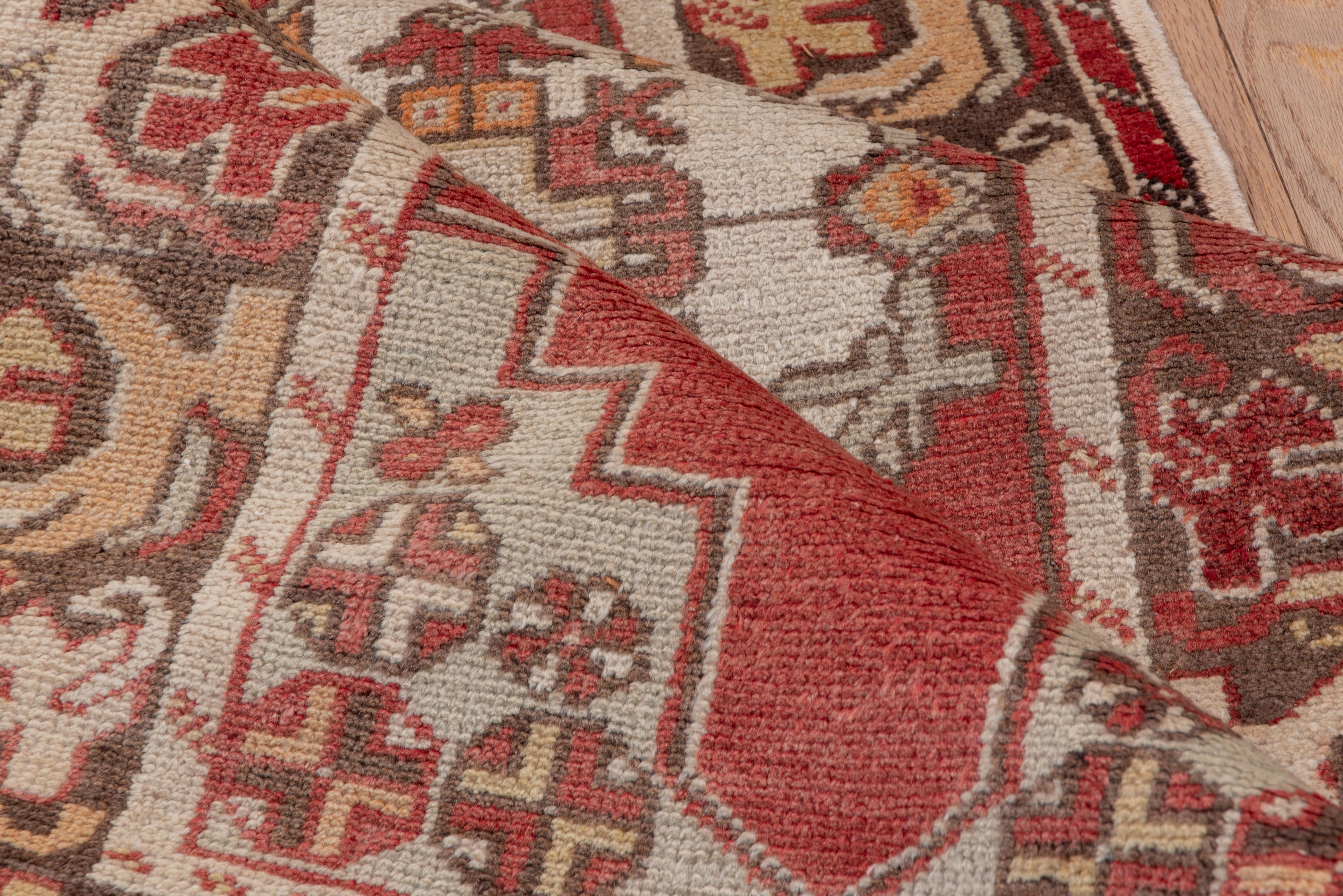 This vintage Oushak runner features a bold series of ivory medallions set against a richly faded brick-red ground. Intricately drawn with angular floral detailing and flanked by stylized rosettes, the design offers a dynamic interplay of symmetry