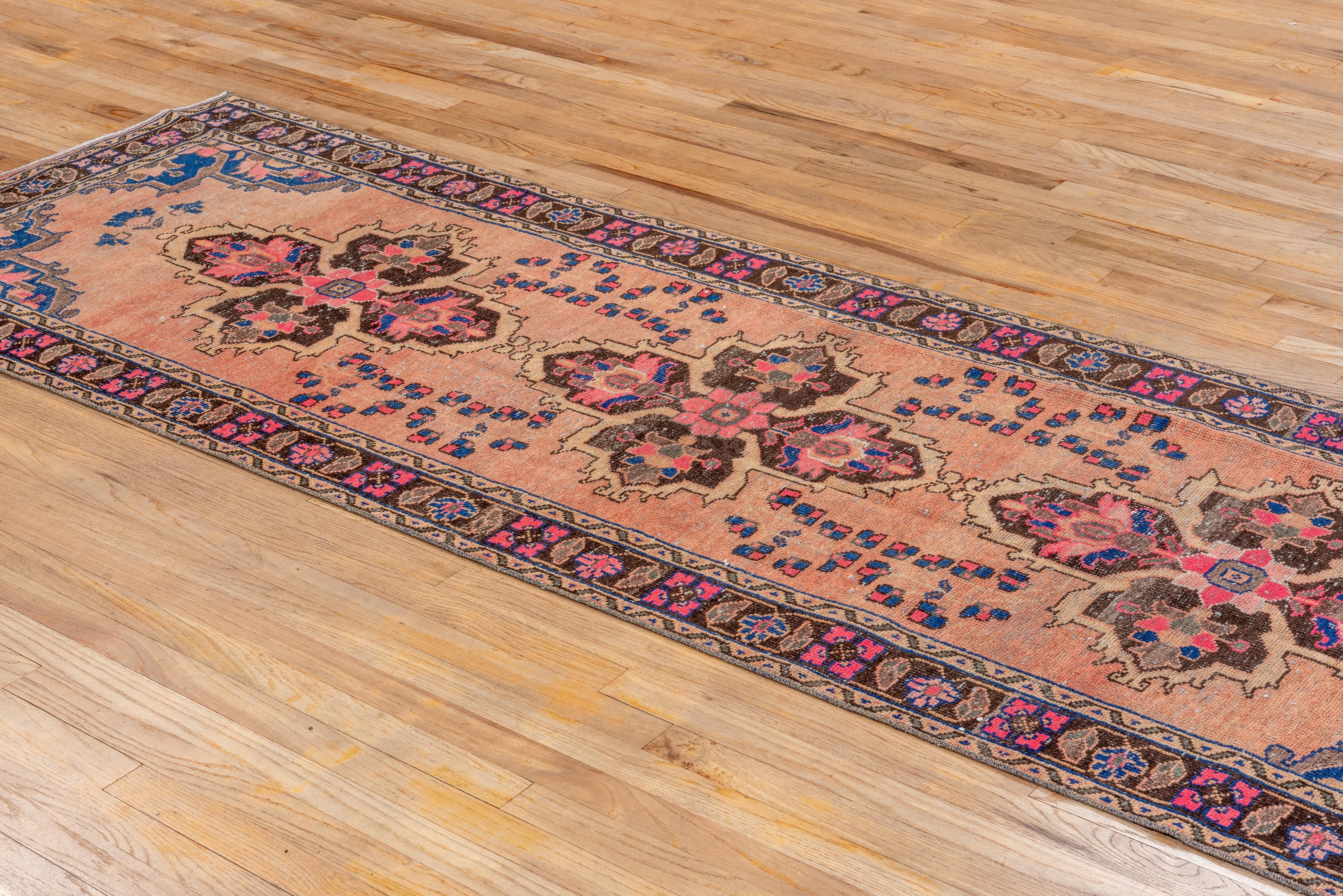 Este elegante camino de mesa vintage de Oushak presenta un cálido campo rosa acentuado por atrevidos medallones florales en marrón intenso, azul zafiro y magenta. Los motivos estilizados de enredaderas y las esquinas angulosas evocan el diseño