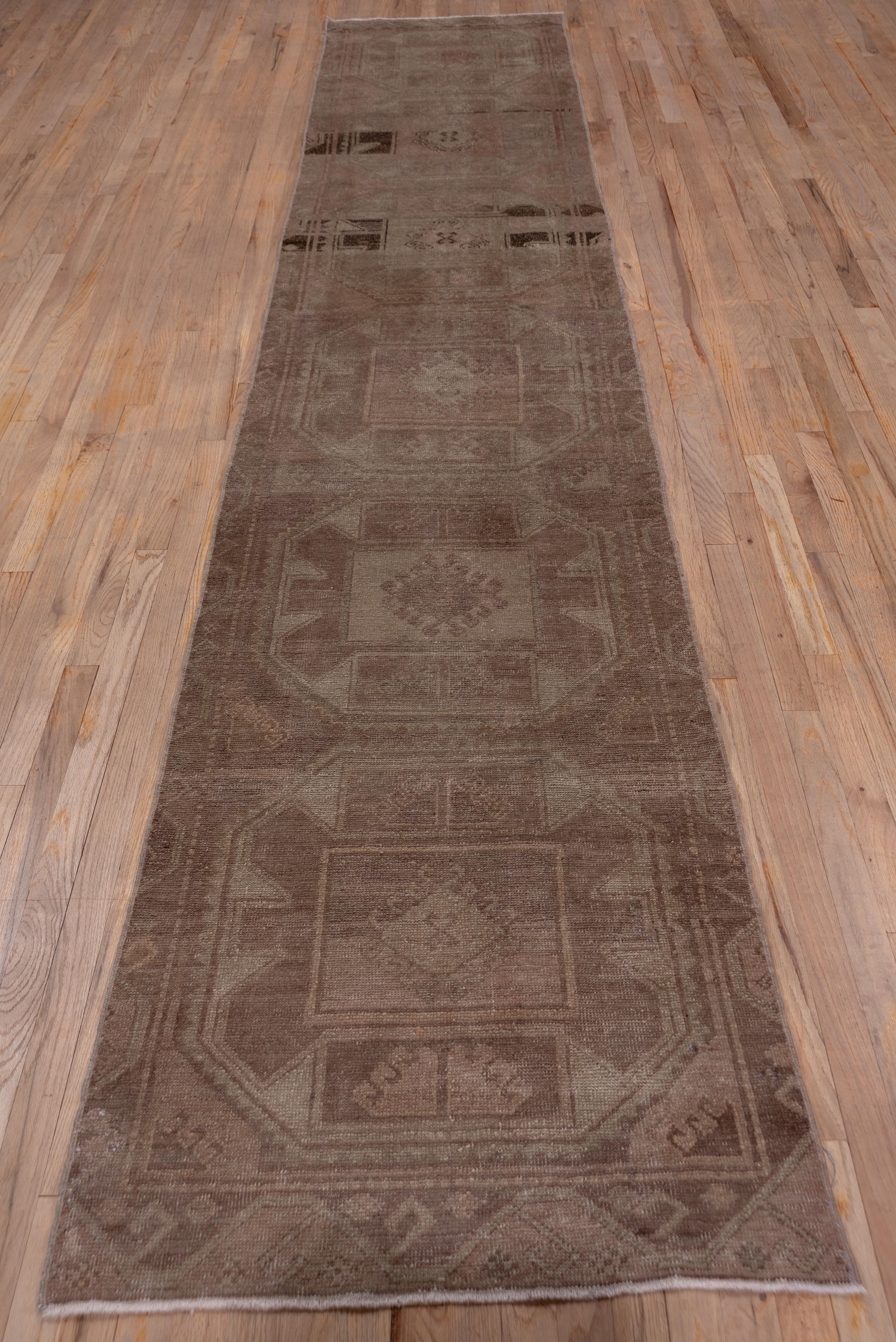 This tone-on-tone eastern Anatolian runner shows a medium brown field closely covered with six octagonal medallions in beige and brown. Dark brown abrash across the entire rug is quite noticeable.