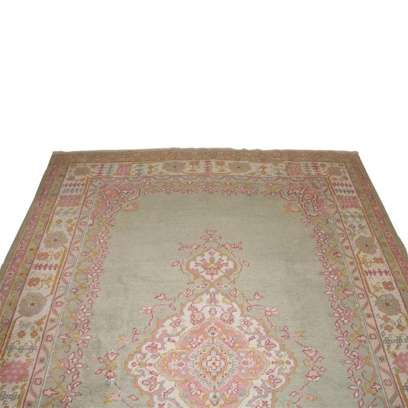 A vintage Oushak carpet circa 1930 with a center medallion on a celadon background with a border of flowers and vines. Serene shades of pinks, yellow and blues create a geometric design.