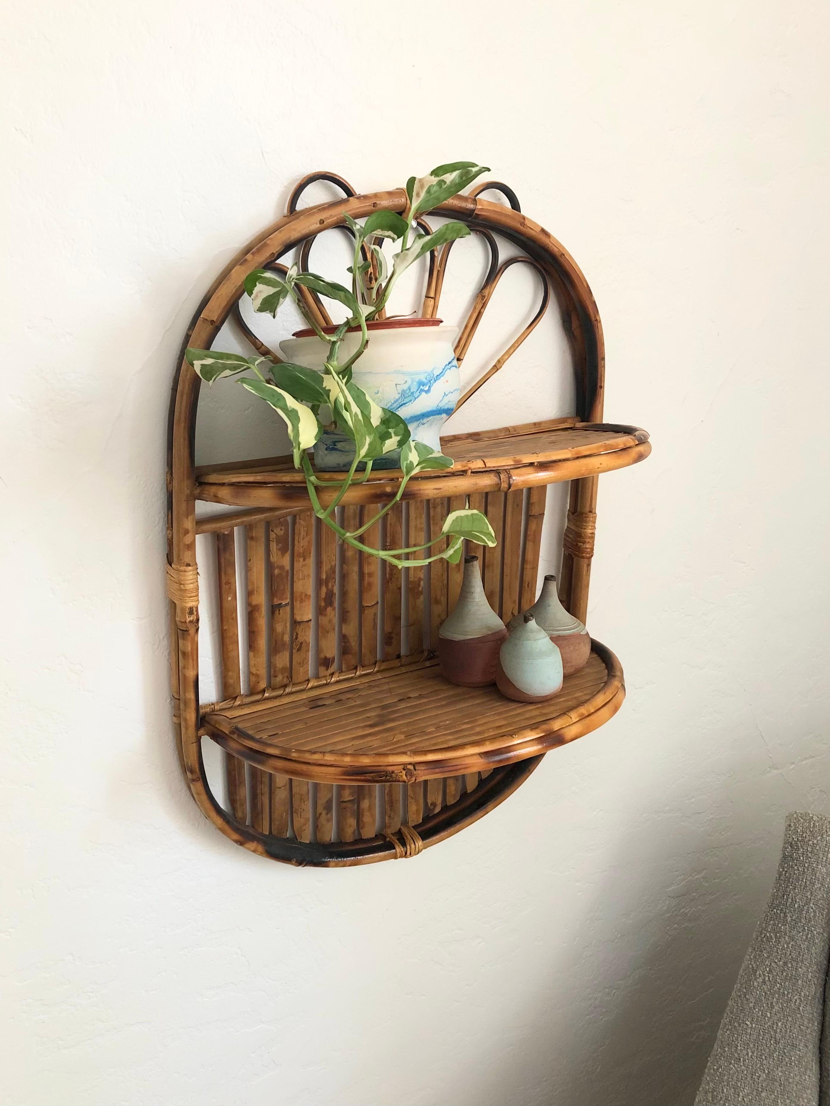 A vintage oval bamboo shelf. Features 2 semi circular bamboo shelves that can fold away to make the shelf flat for storage. Perfect for displaying small plants or decorative items.